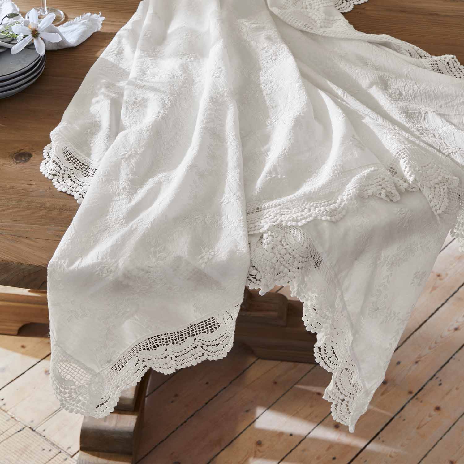 Mantel blanco bordado con borde de encaje sobre mesa de madera, decoración de mesa elegante