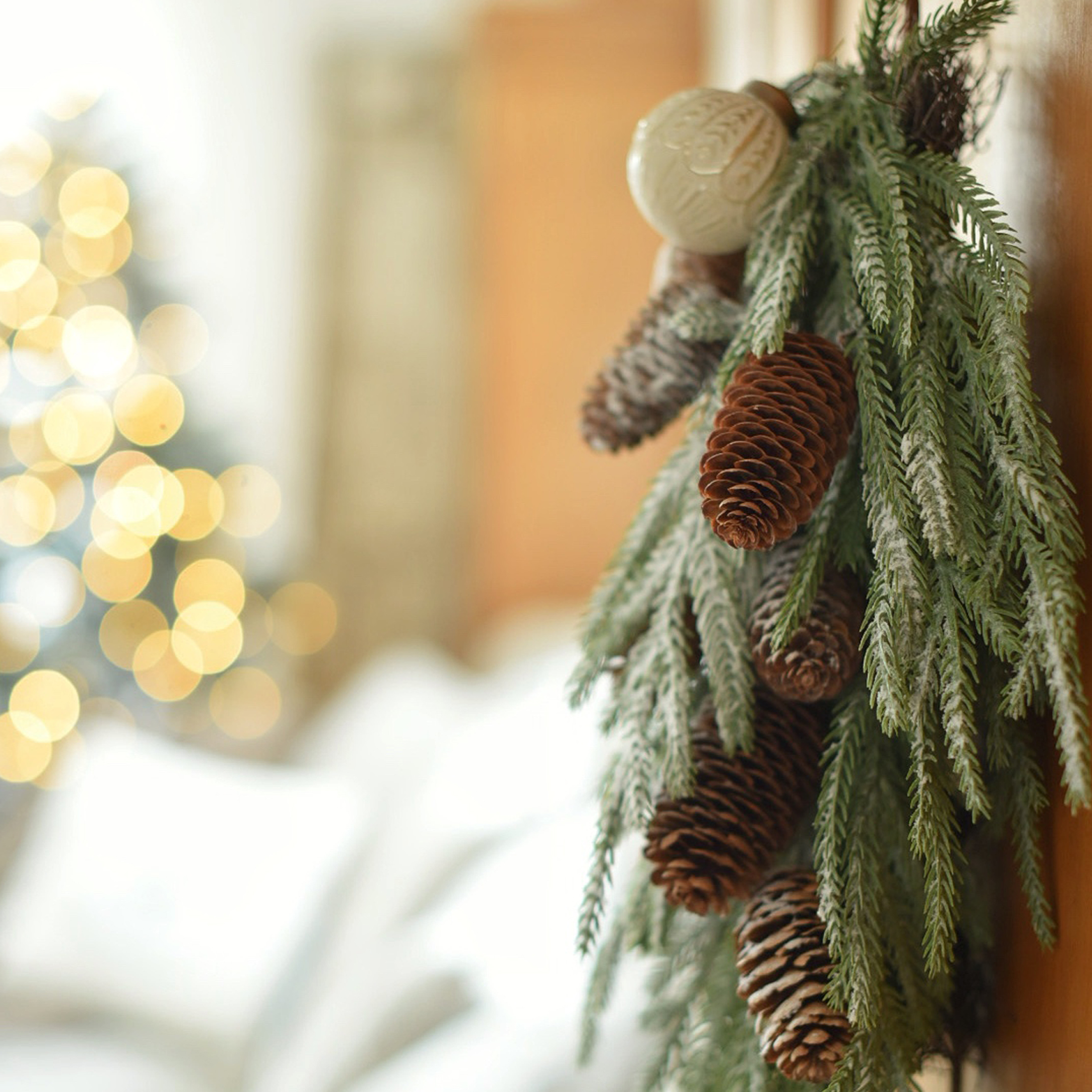 Decoración navideña con ramas verdes y piñas marrones sobre fondo de luces desenfocadas