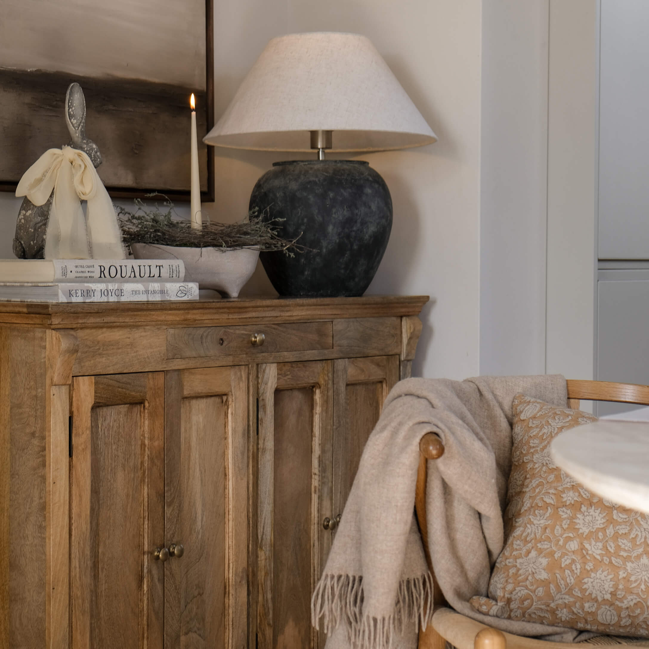 Aparador de madera con lámpara de cerámica, vela encendida y decoración en salón acogedor