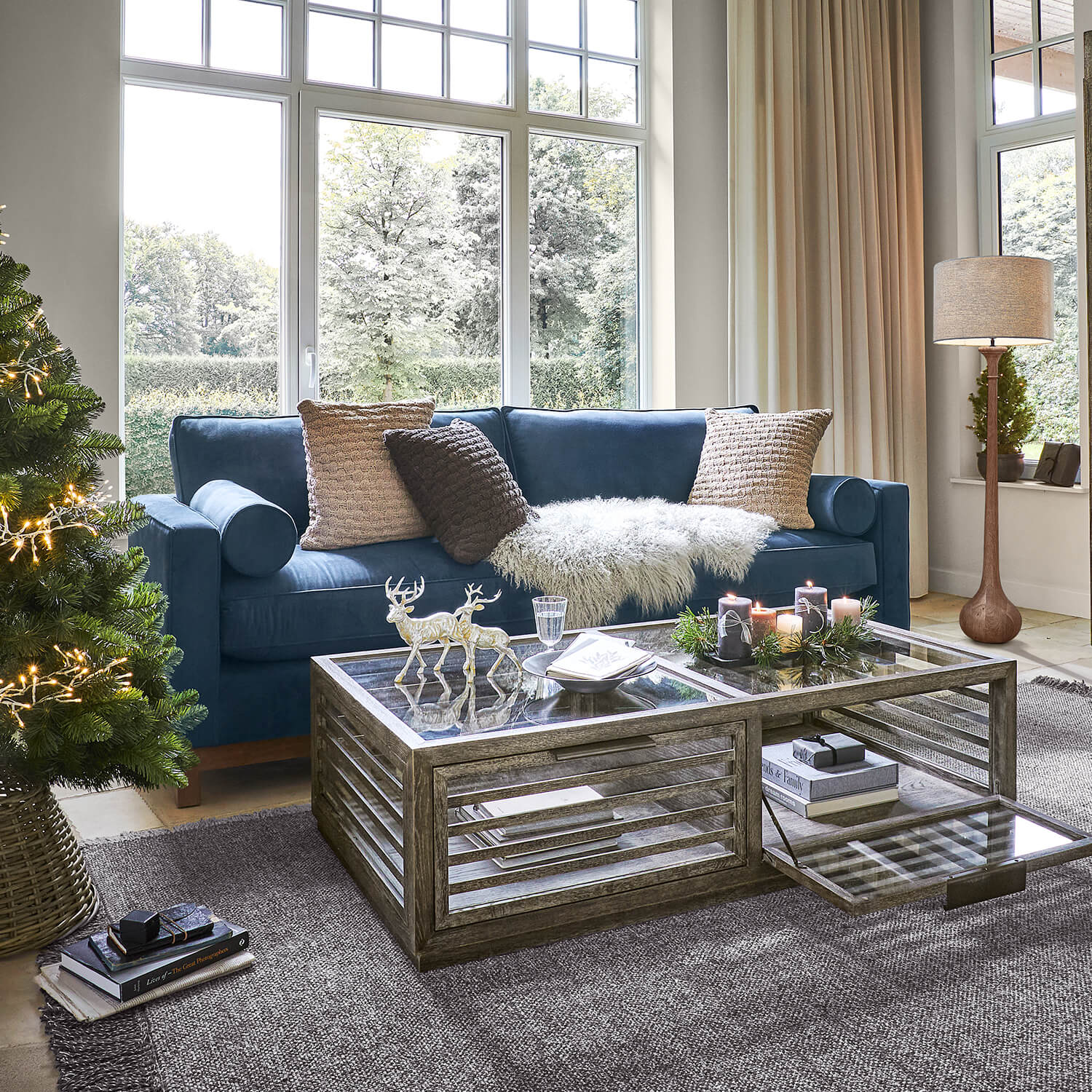 Sala acogedora con sofá azul marino, mesa de centro de cristal y decoración navideña con árbol y velas