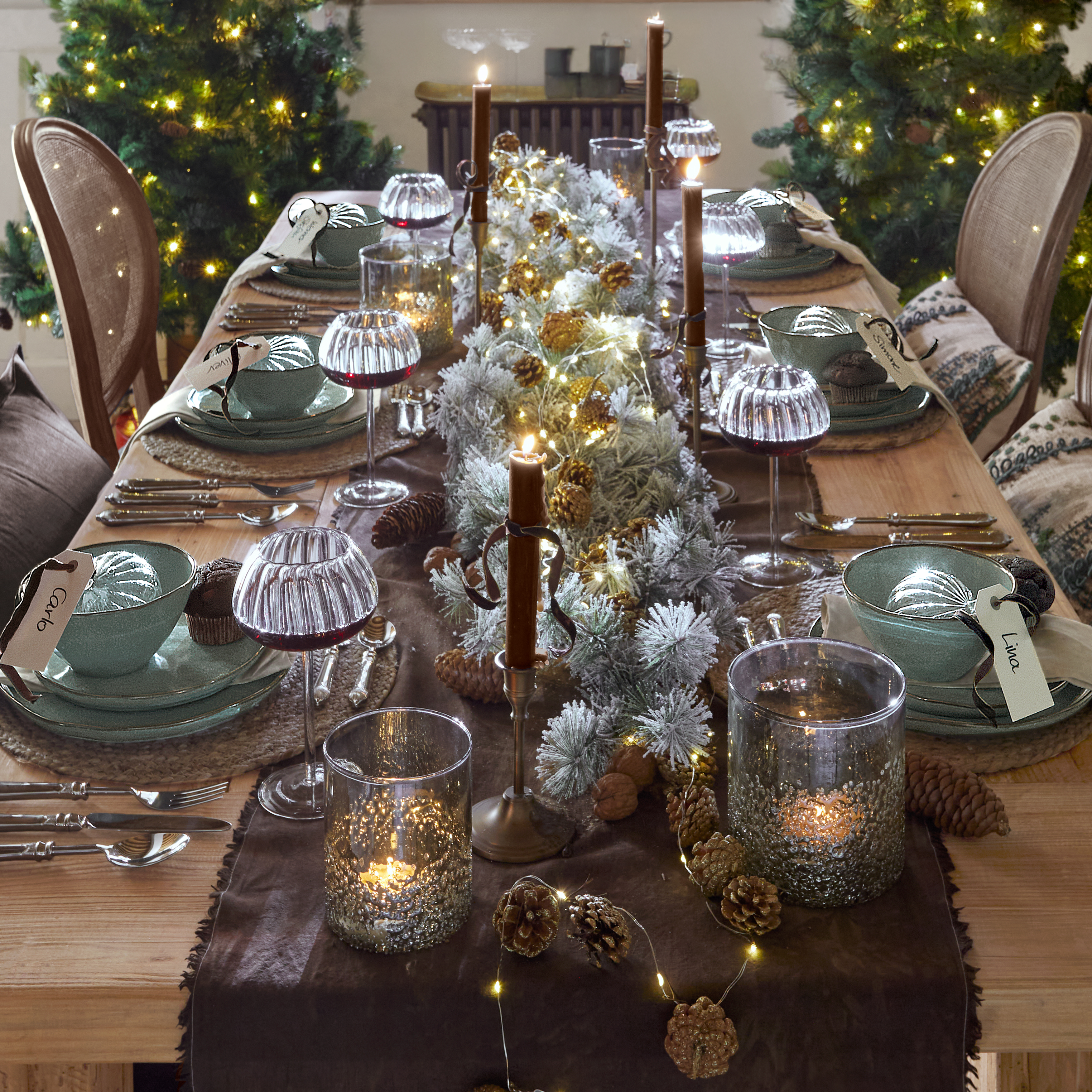 Mesa navideña con vajilla de cerámica verde, velas encendidas y luces LED sobre mesa de madera