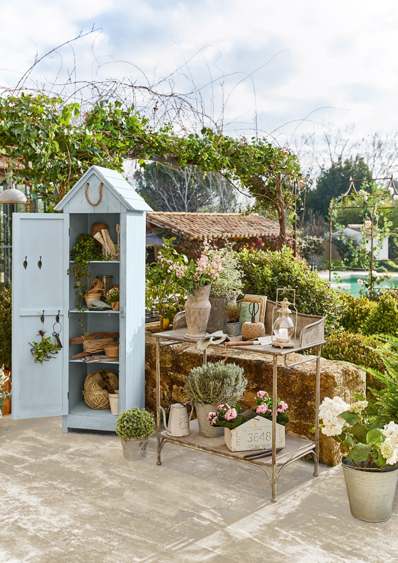 Armario de jardín de madera azul con estantes y mesa de metal con flores y herramientas de jardinería