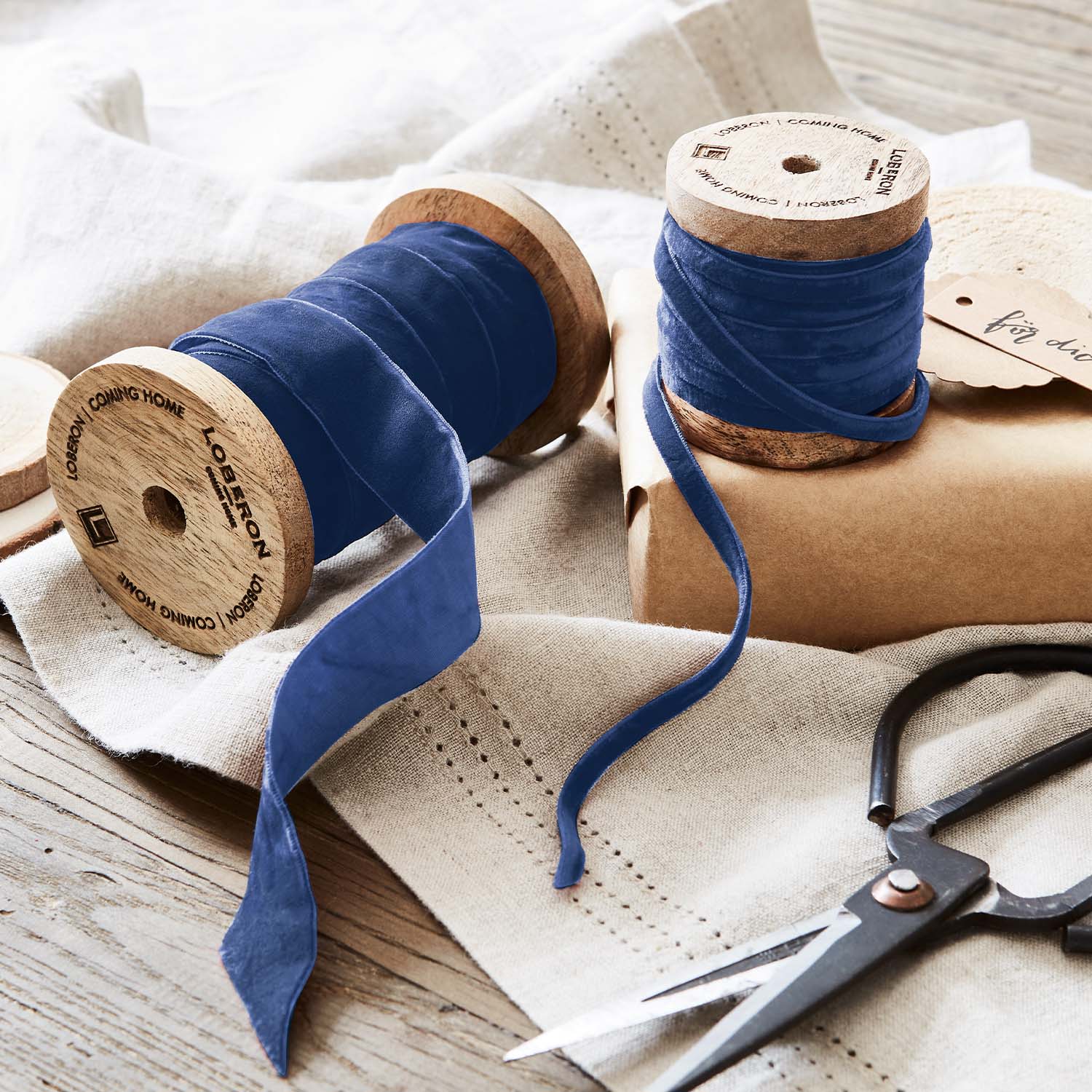 Cinta de terciopelo azul en carretes de madera con tijeras sobre tela de lino para decoración y manualidades