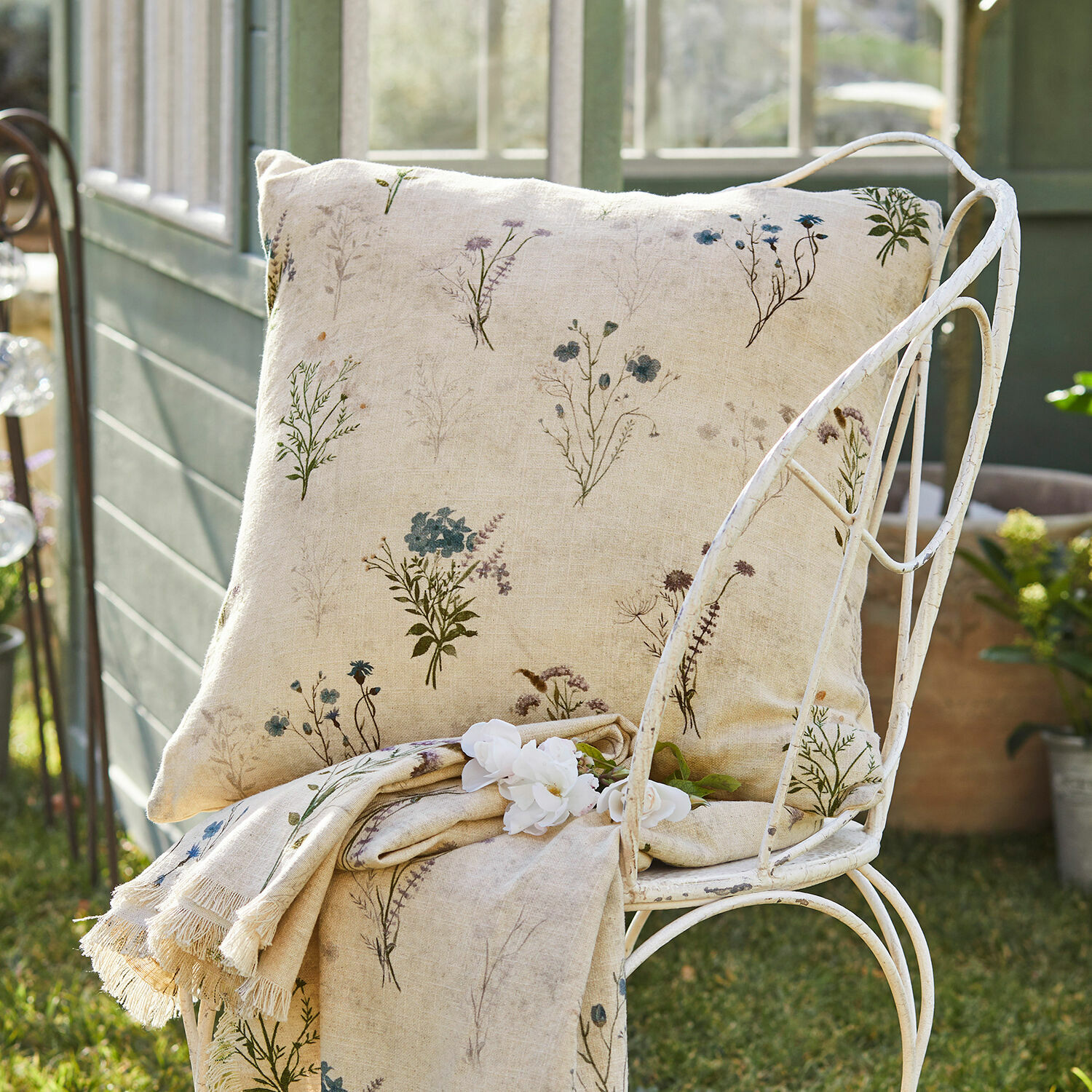 Funda de cojín Cabinda Cojín y manta de lino beige con delicado estampado floral sobre silla metálica en jardín