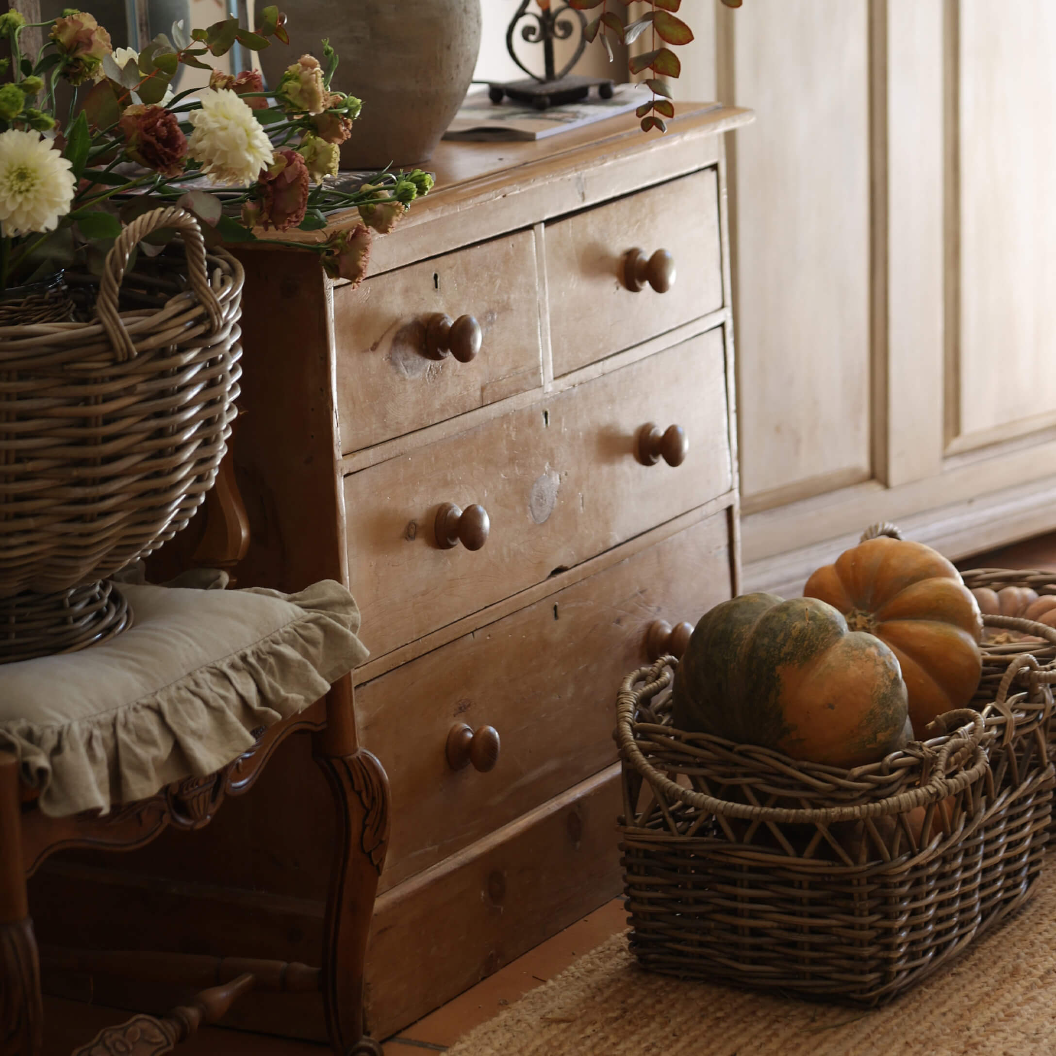 Cómoda rústica de madera con cuatro cajones y cesta de mimbre con calabazas en interior acogedor