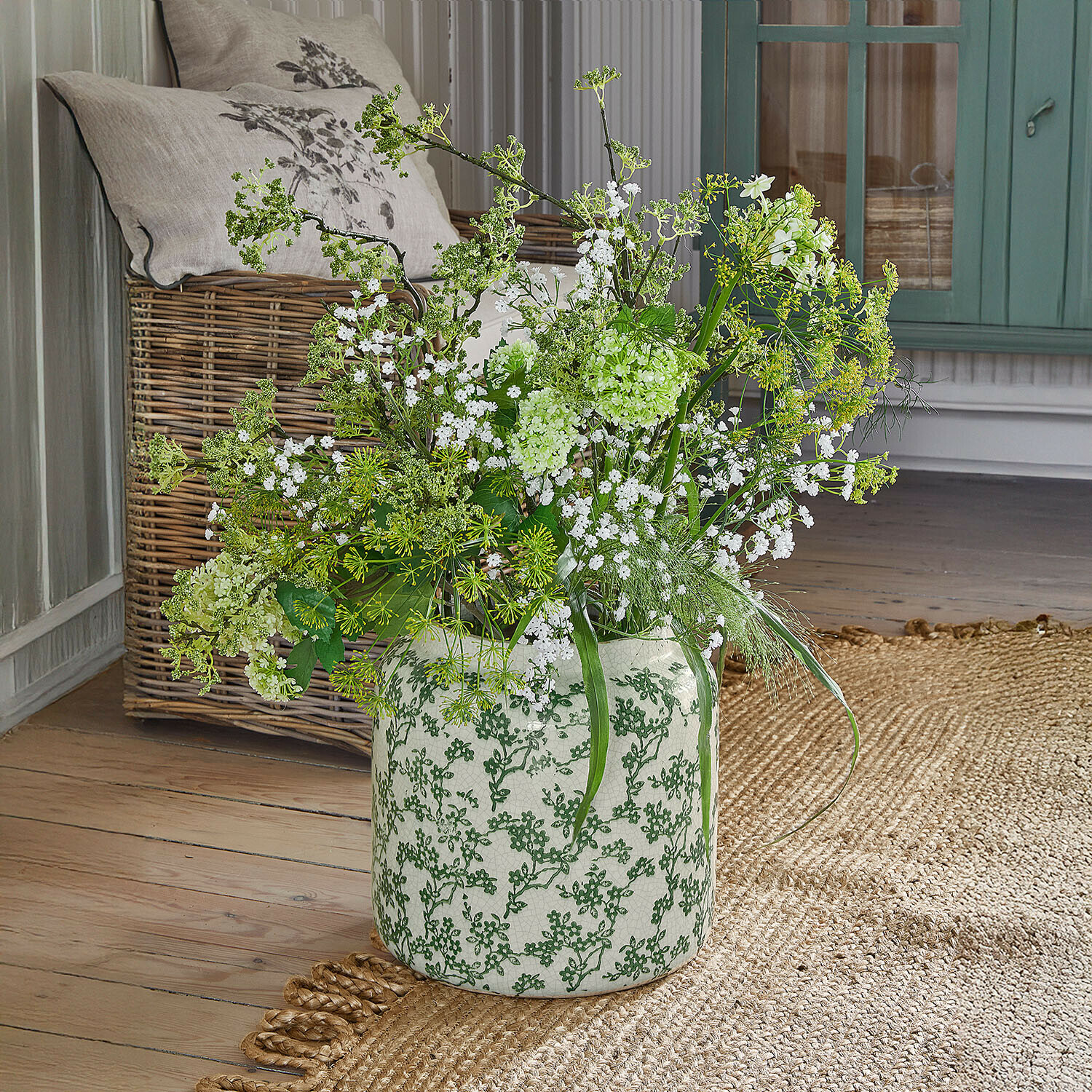 Jarrón Vaudrisse Jarrón de cerámica blanca con diseño verde, flores blancas y ramas verdes sobre suelo de madera