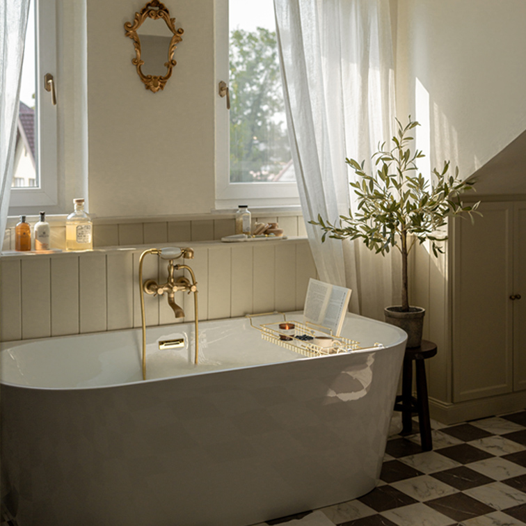 Bañera independiente blanca con grifería de latón y espejo decorativo en baño luminoso con planta