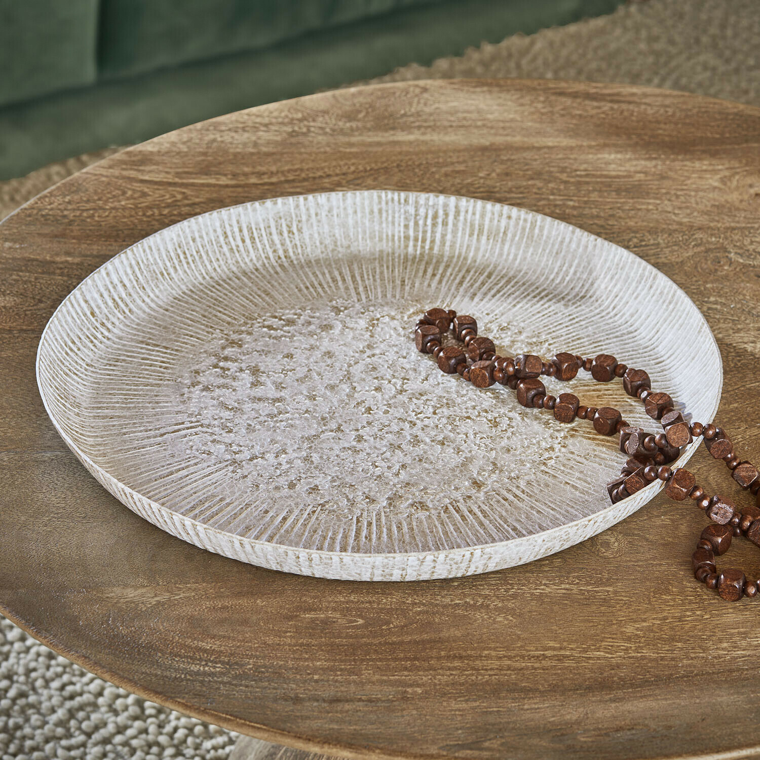 Bandeja Gravière Bandeja decorativa redonda de madera blanca con textura sobre mesa de madera con collar marrón