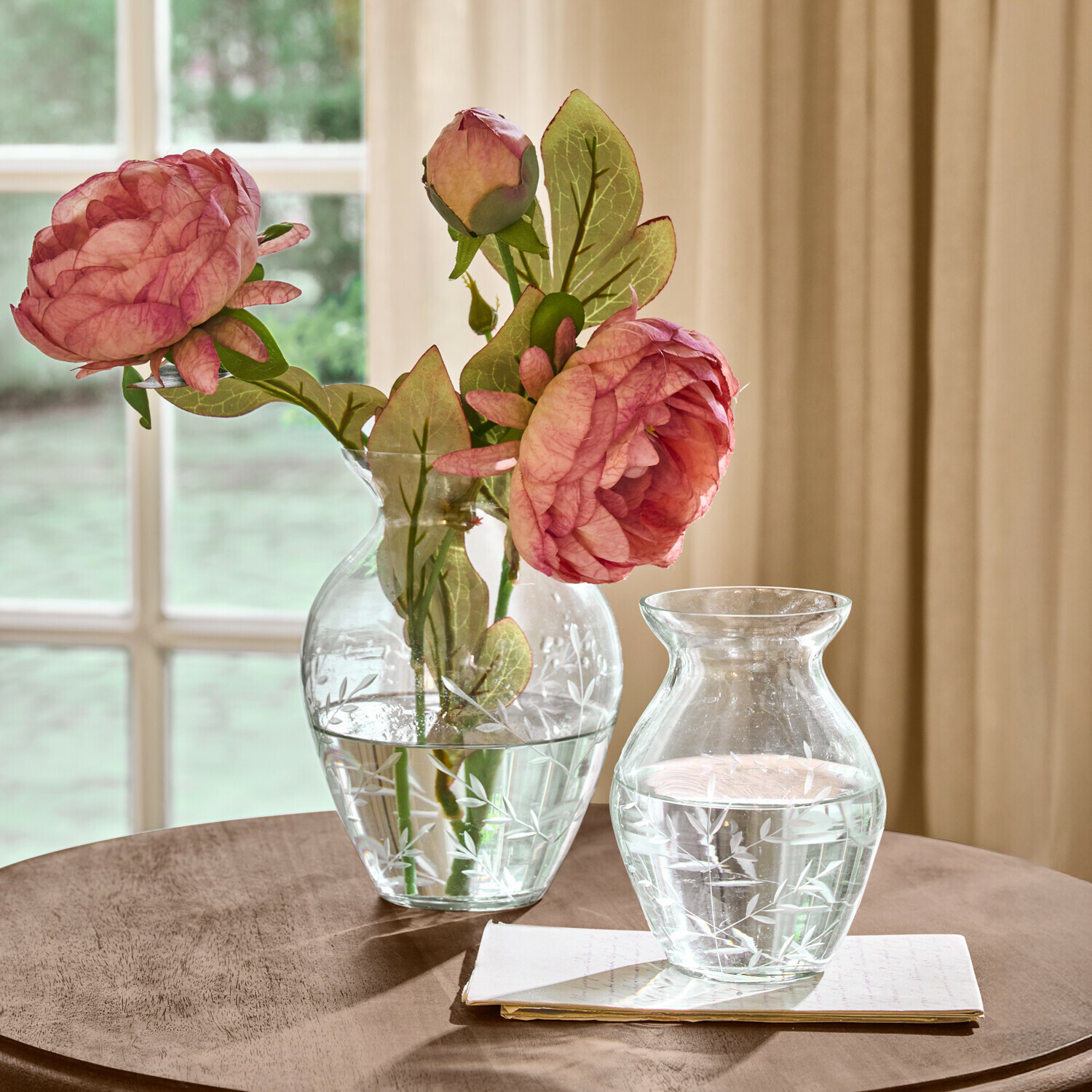 Set de 2 jarrones Paimpont Jarrones de vidrio transparente con diseño grabado de hojas, uno con flores rosas, sobre mesa de madera