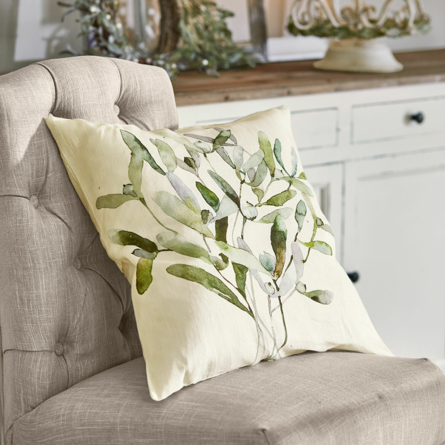 Funda de cojín Mistletoe Cojín beige con estampado de hojas verdes sobre silla gris en estilo natural