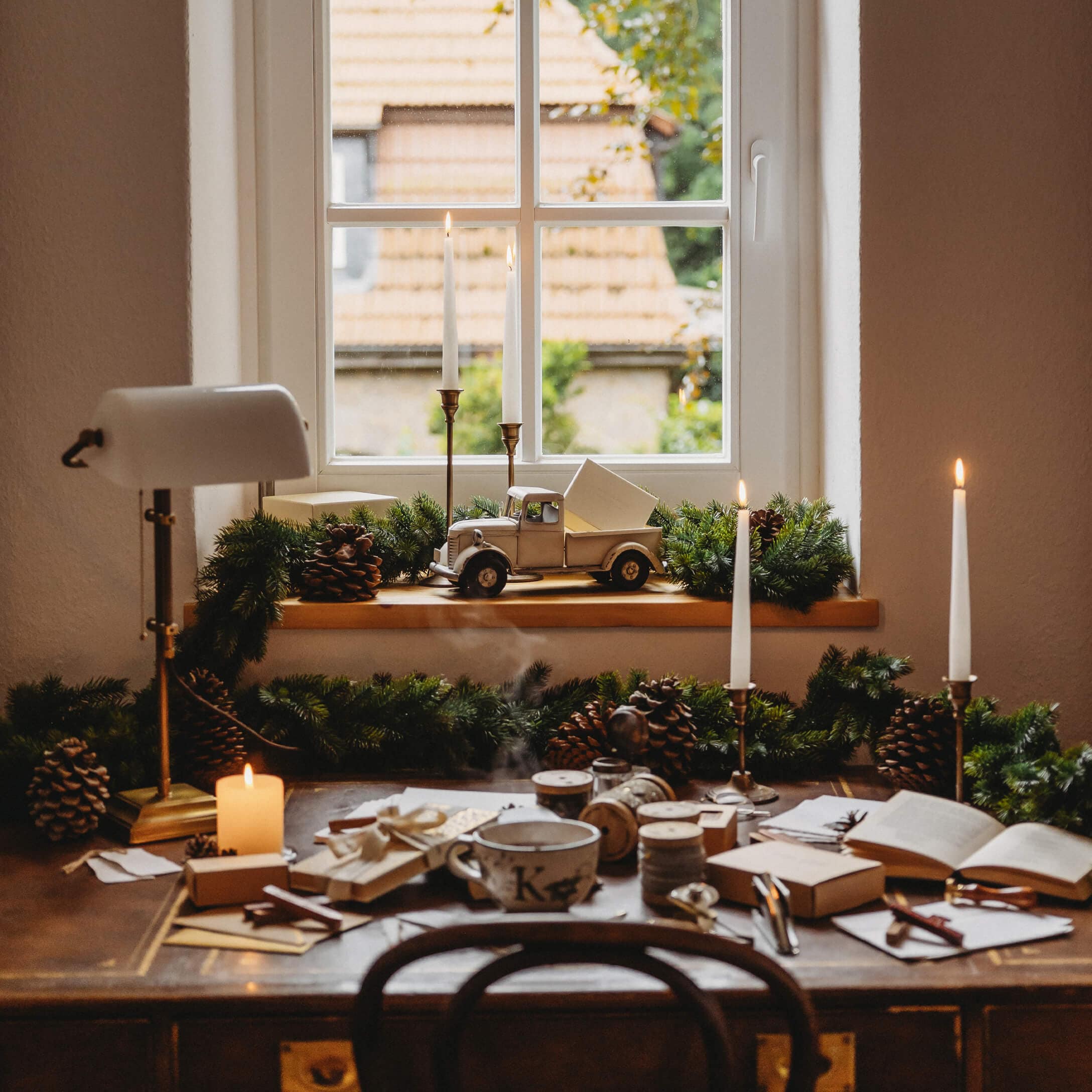 Mesa rústica de madera con velas y decoración navideña junto a ventana con vista a tejados