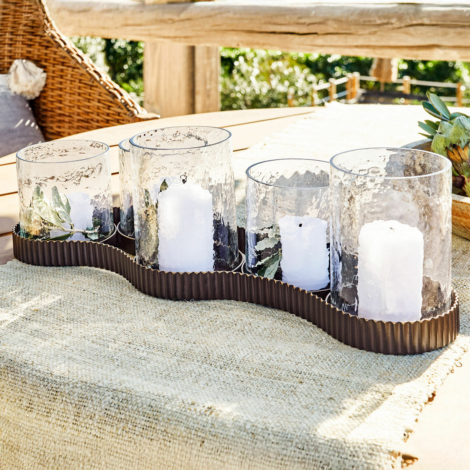 Farol Méridienn Conjunto de 5 portavelas de vidrio con velas blancas en base metálica marrón sobre mesa de jardín