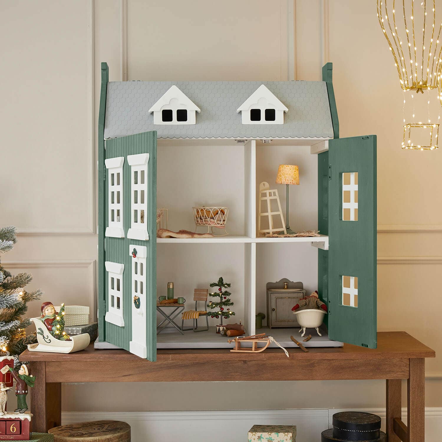 Casa de muñecas de madera verde y gris con puertas abiertas y decoración navideña en su interior