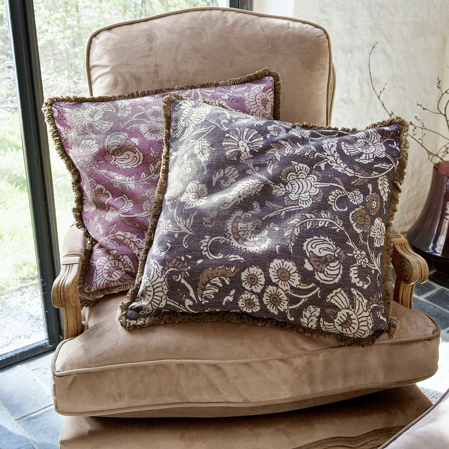 Set de 2 fundas de cojín Lalluga Dos cojines decorativos con diseño floral en tonos morado y gris sobre un sillón beige
