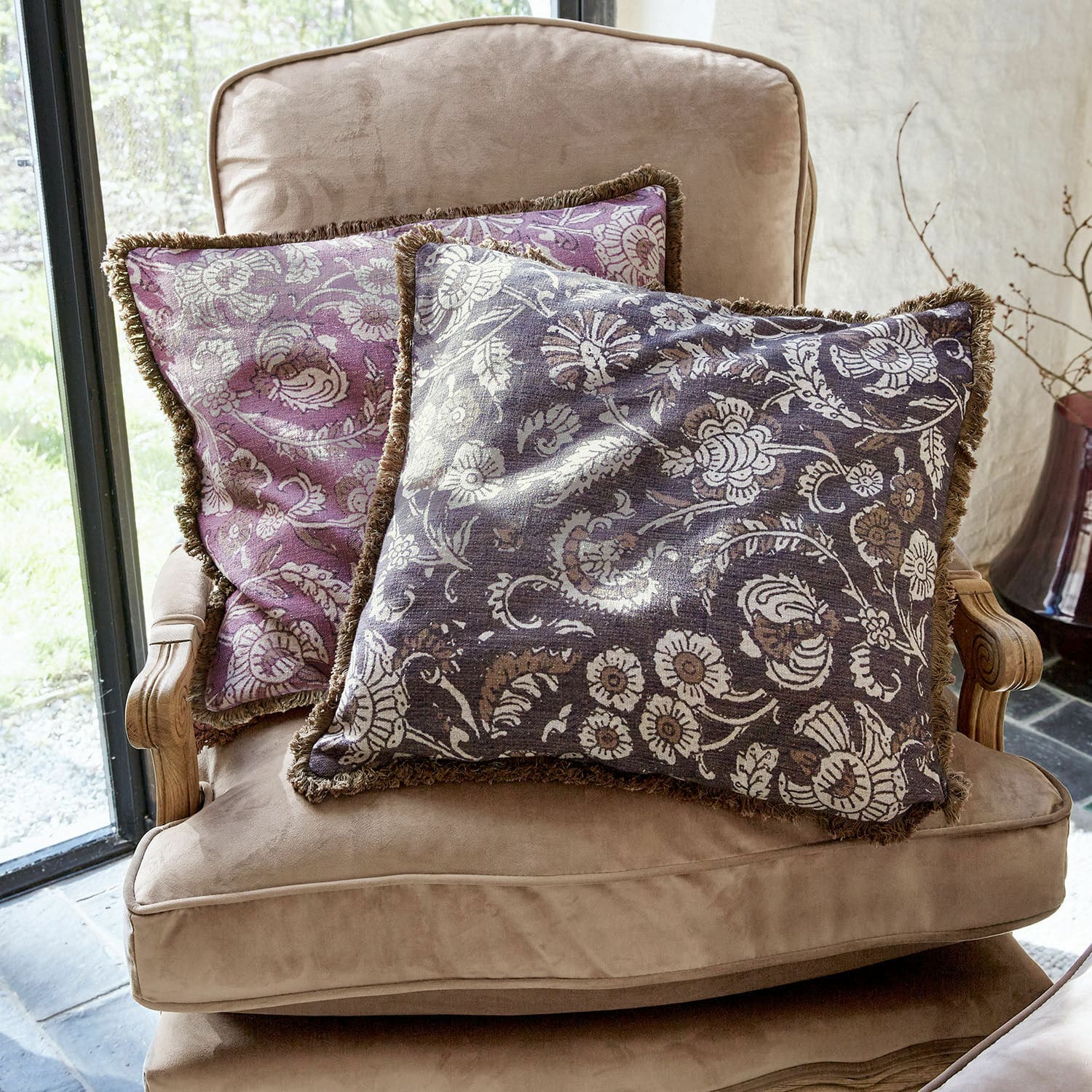 Set de 2 fundas de cojín Lalluga Dos cojines decorativos con diseño floral en tonos morado y gris sobre un sillón beige