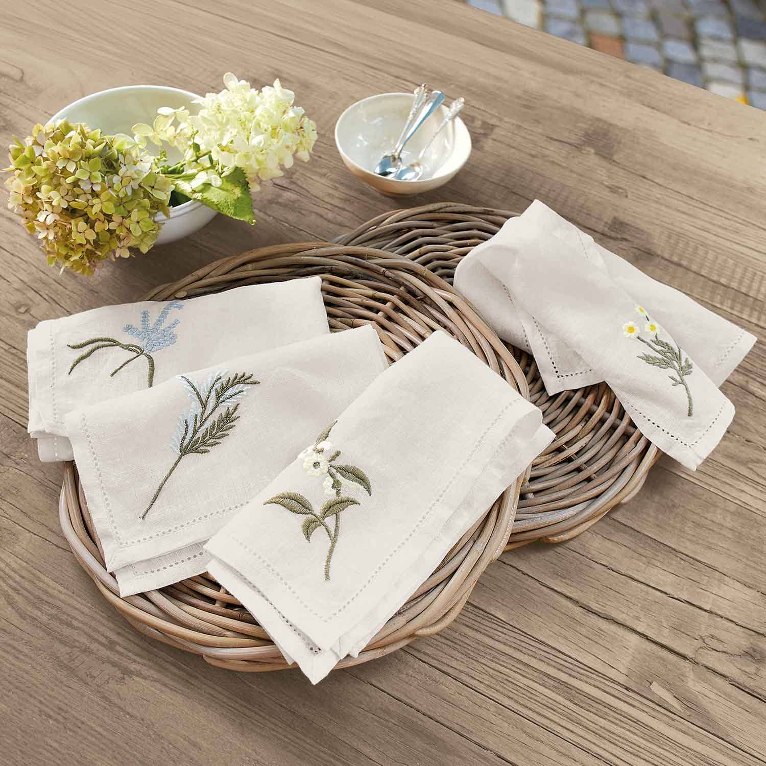 Servilletas de lino crema con bordados florales sobre bandeja de mimbre en mesa de madera