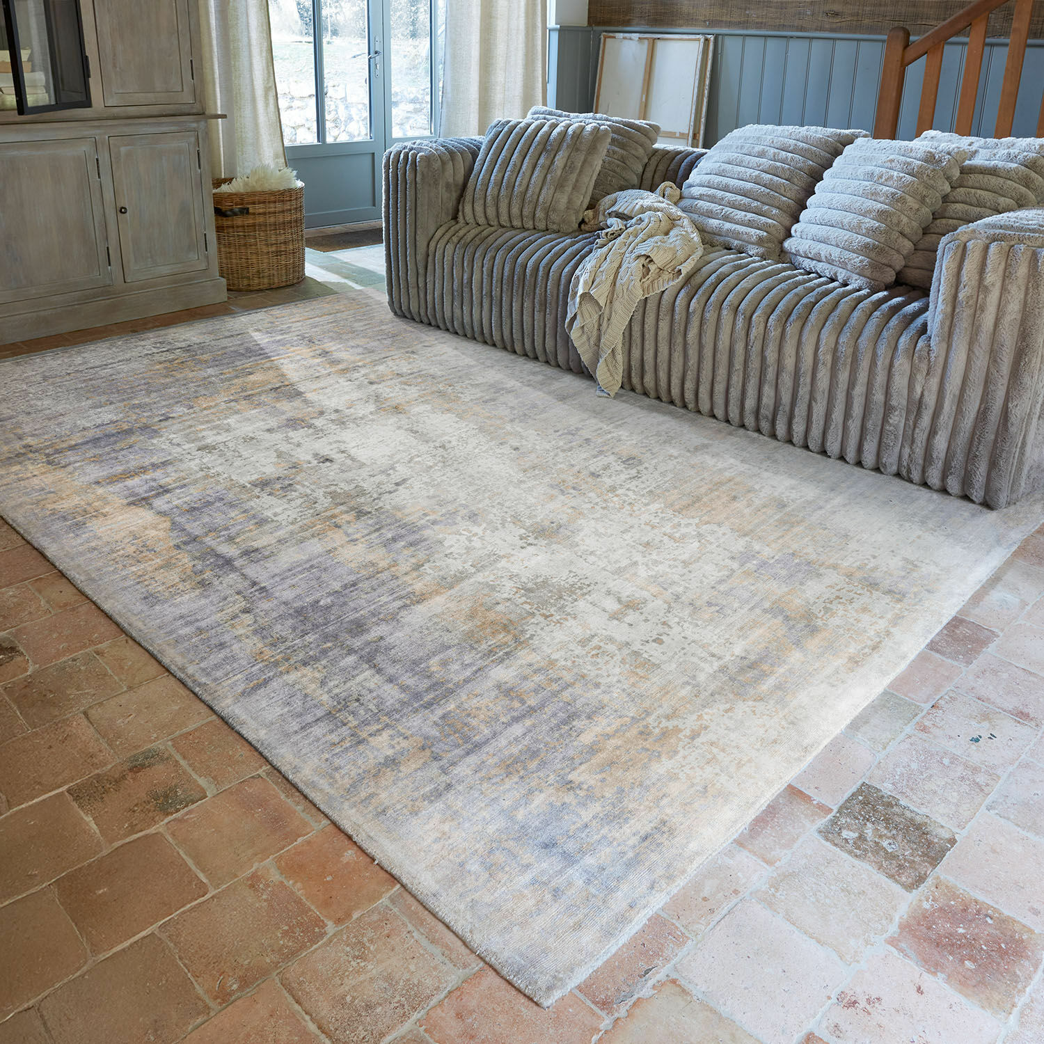 Alfombra Qalheera Alfombra decorativa en tonos beige y gris bajo un sofá gris en sala de estar
