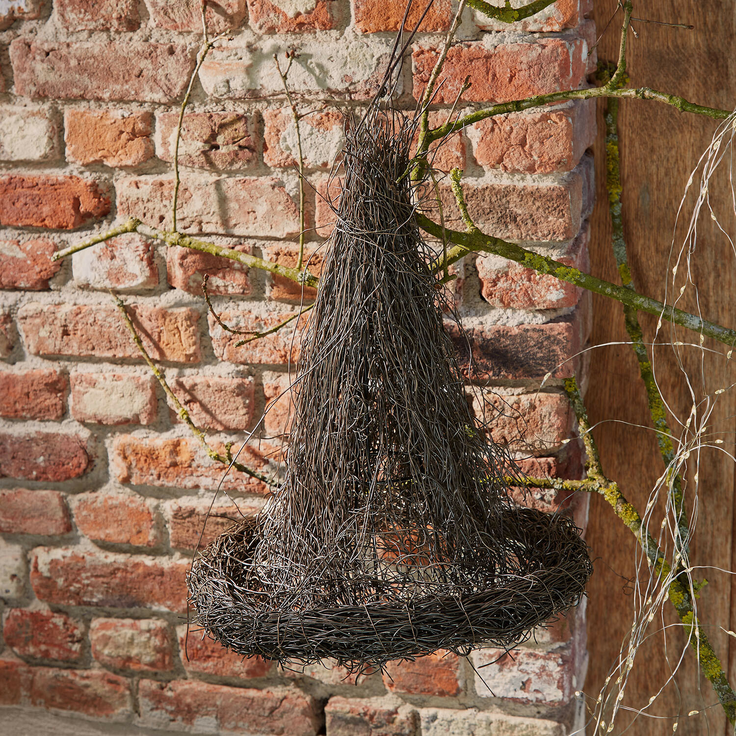 Sombrero decorativo Talmora Decoración colgante de alambre negro con forma de sombrero de bruja frente a pared de ladrillo