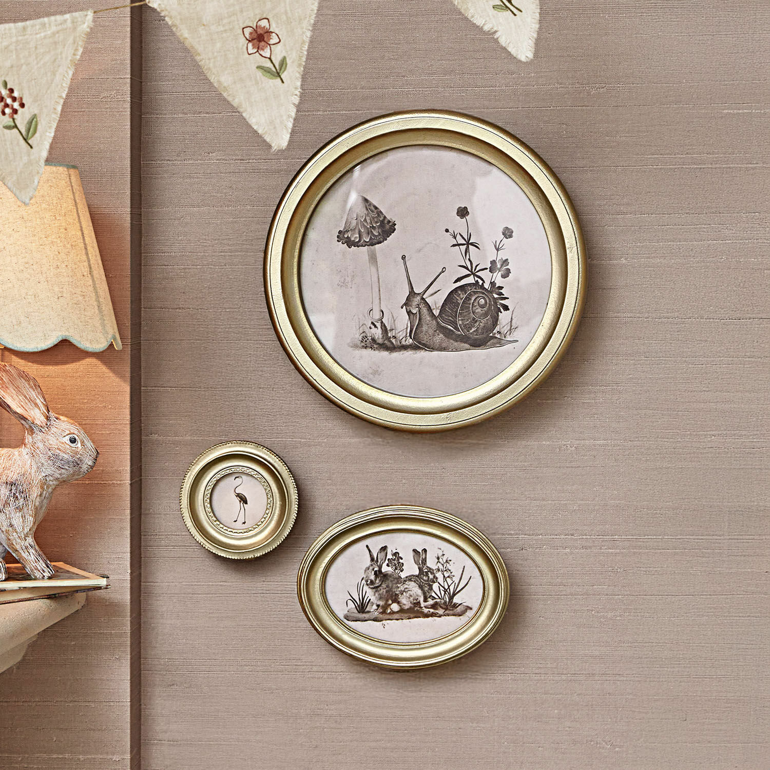 Set de 3 cuadros Atriana Conjunto de tres marcos dorados con ilustraciones en blanco y negro de animales y plantas en pared beige.