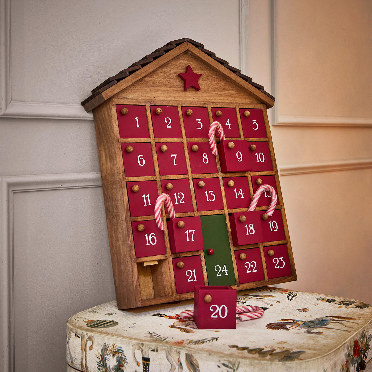 Calendario de adviento de madera en forma de casa con puertas rojas y número 24 verde, decorado con bastones de caramelo