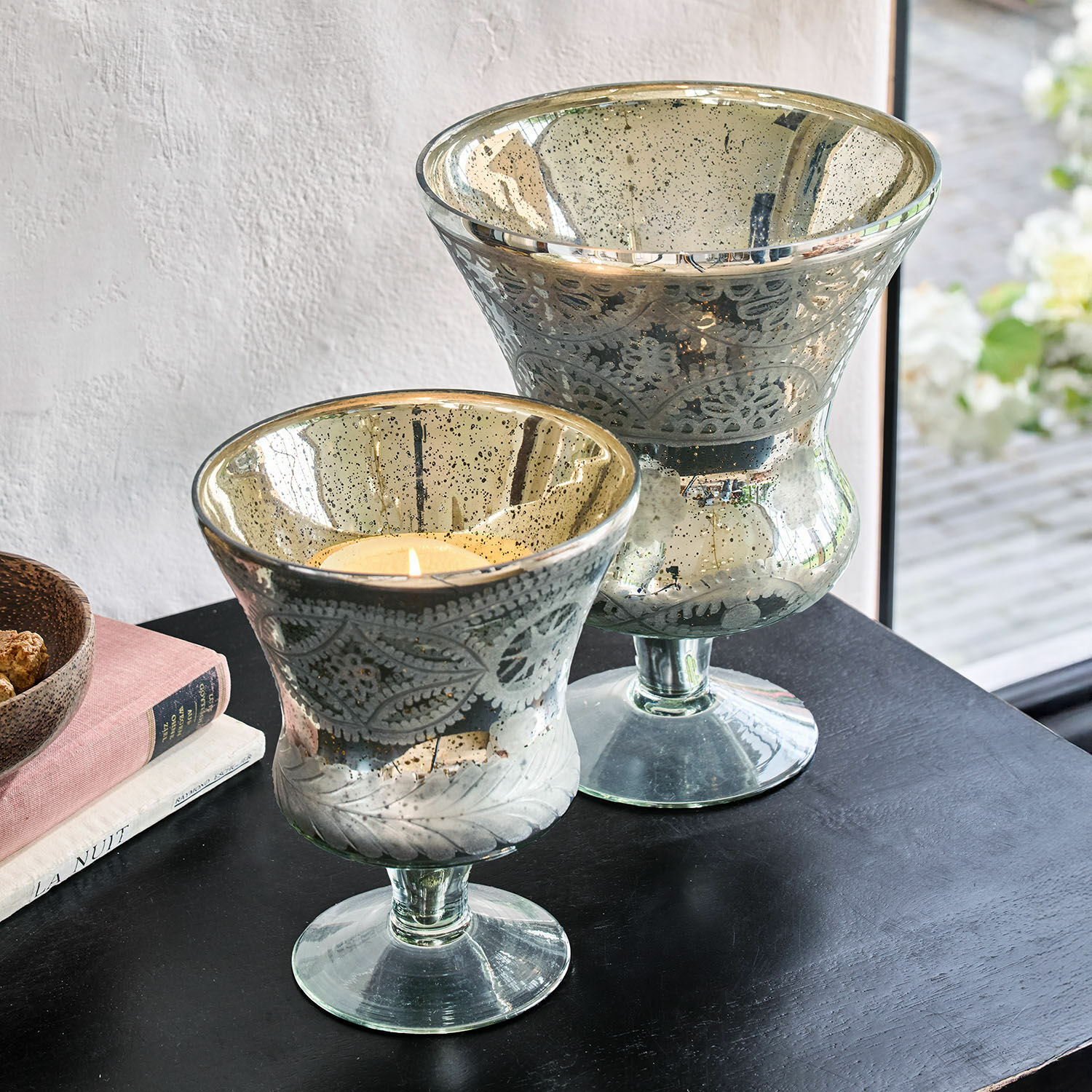 Set de 2 portavelas Zorayne Dos portavelas decorativos de vidrio con diseño de hojas y acabado plateado sobre mesa negra