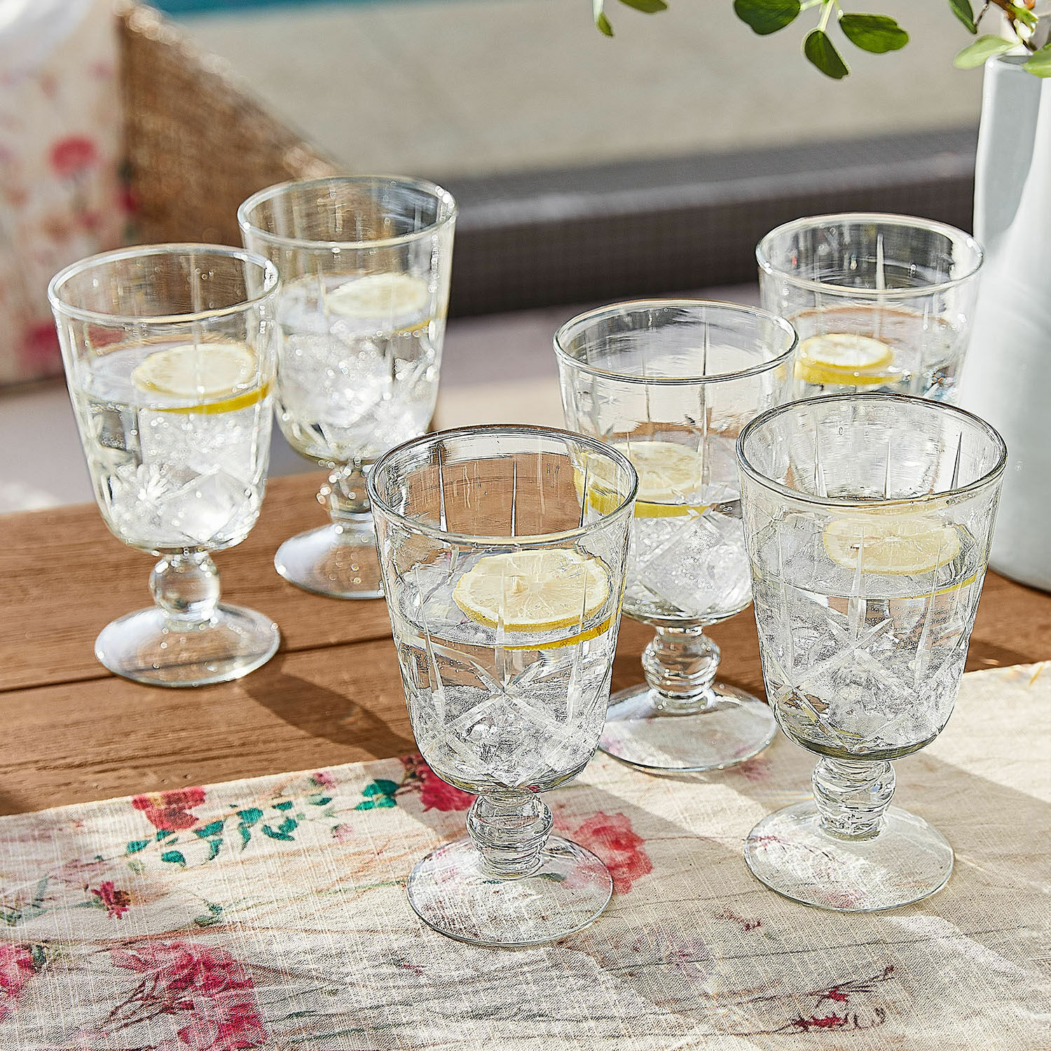 Set de 6 vasos Mirathor Conjunto de seis vasos transparentes con pie, agua, hielo y rodaja de limón sobre mesa de madera