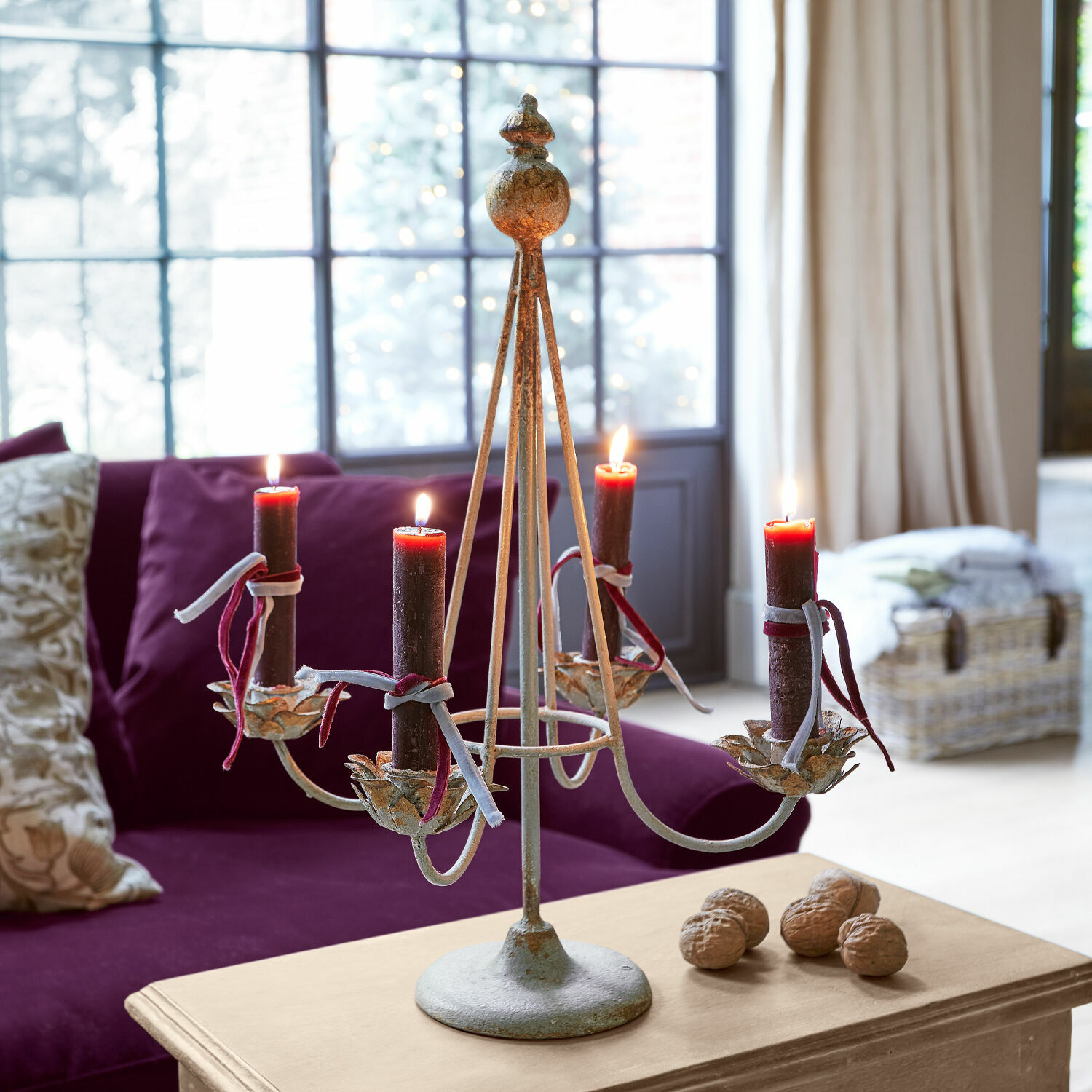 Portavelas Liyanah Candelabro de metal con cuatro velas rojas sobre mesa de madera en sala con sofá morado