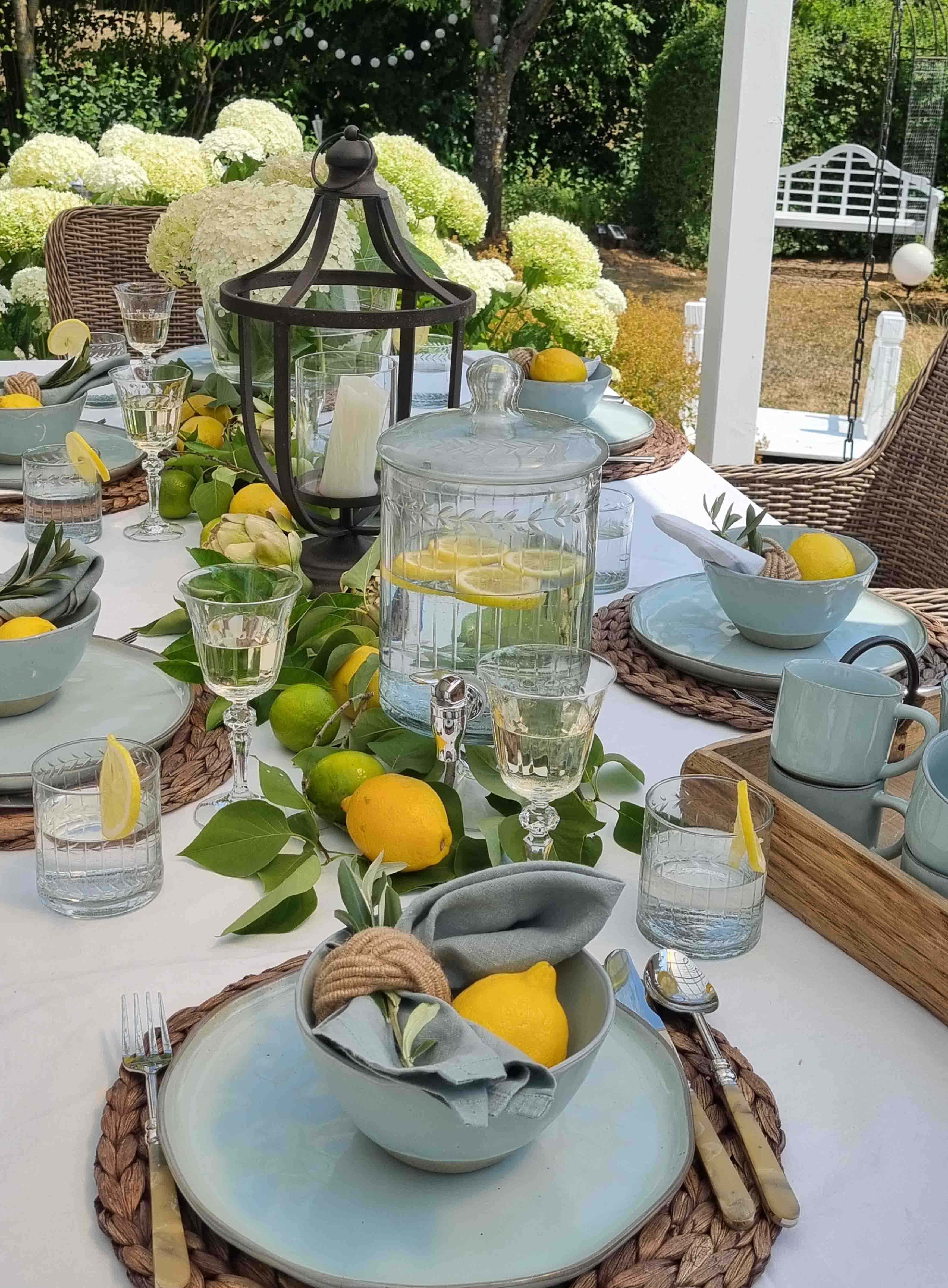 Mesa de jardín de verano con cerámica azul, limones y linterna, flores blancas de fondo