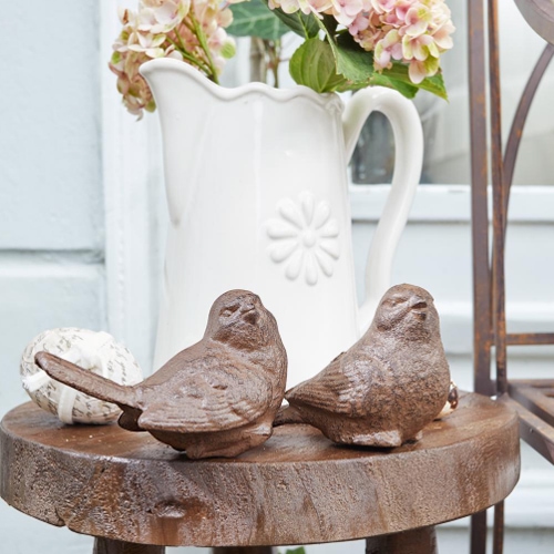 Pájaros decorativos de hierro fundido marrón sobre mesa de madera con jarra blanca al fondo