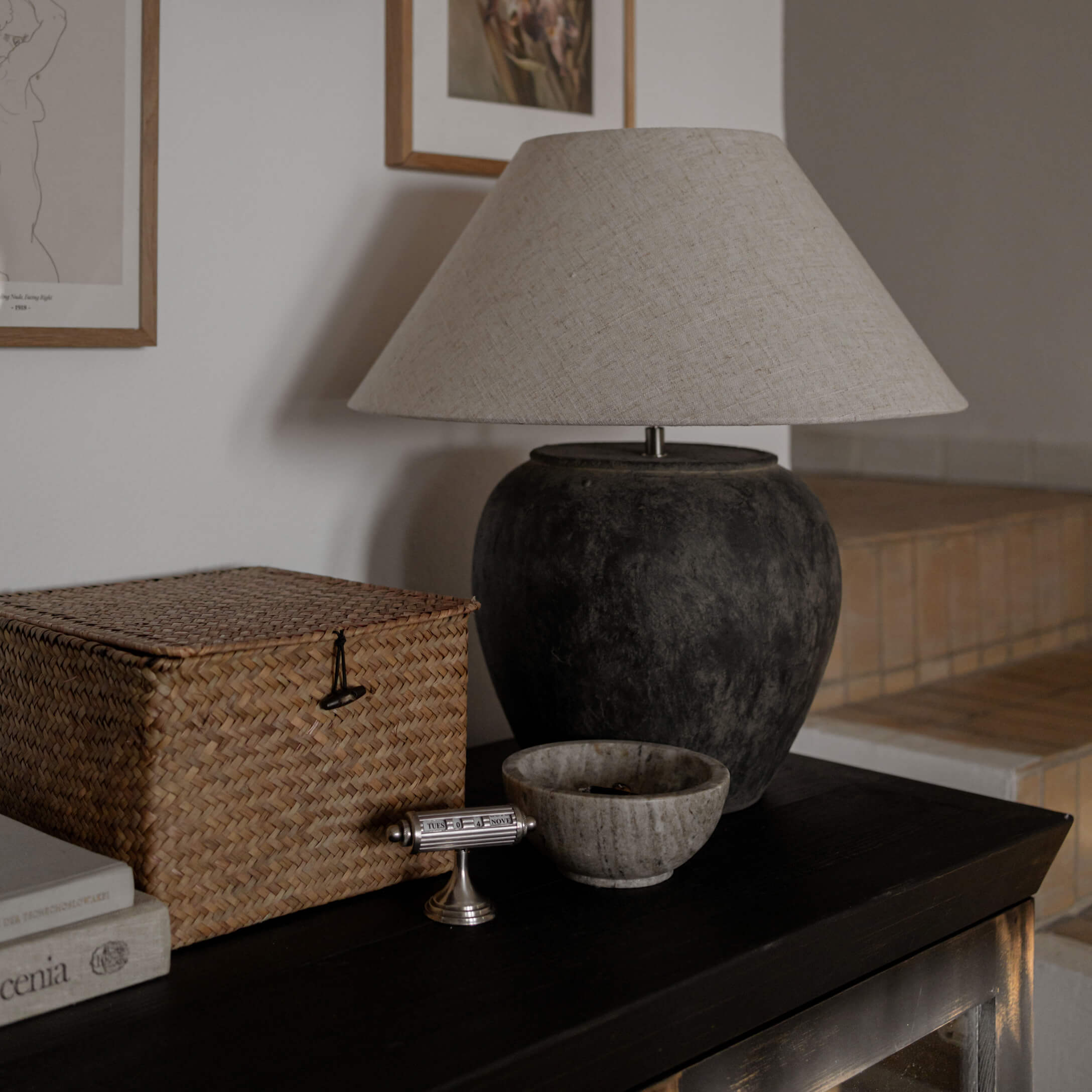 Lámpara de mesa con base de cerámica negra y pantalla beige sobre mesa oscura en salón