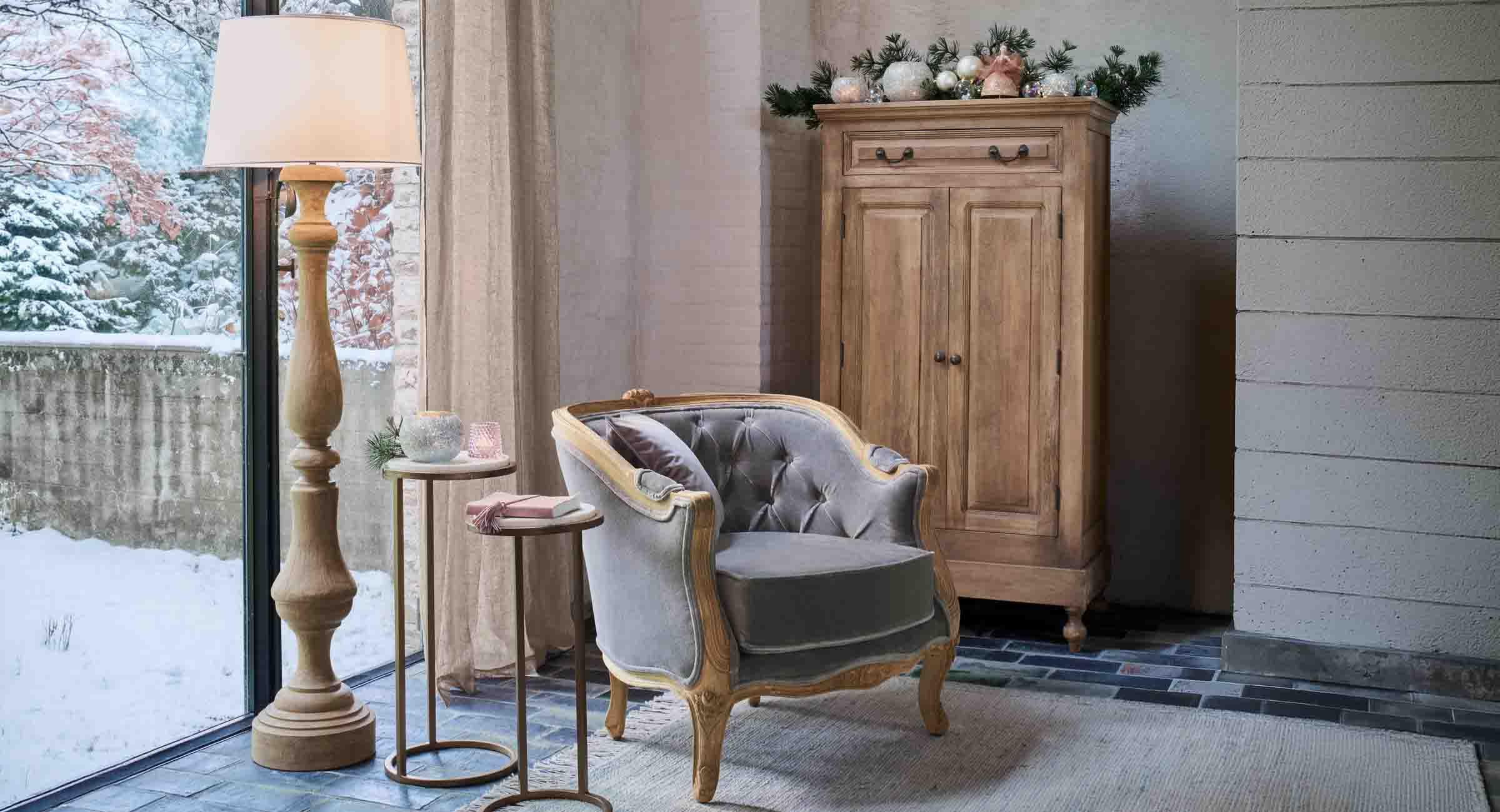 Rincón acogedor con sillón de terciopelo gris y lámpara de pie de madera junto a ventana con vista nevada