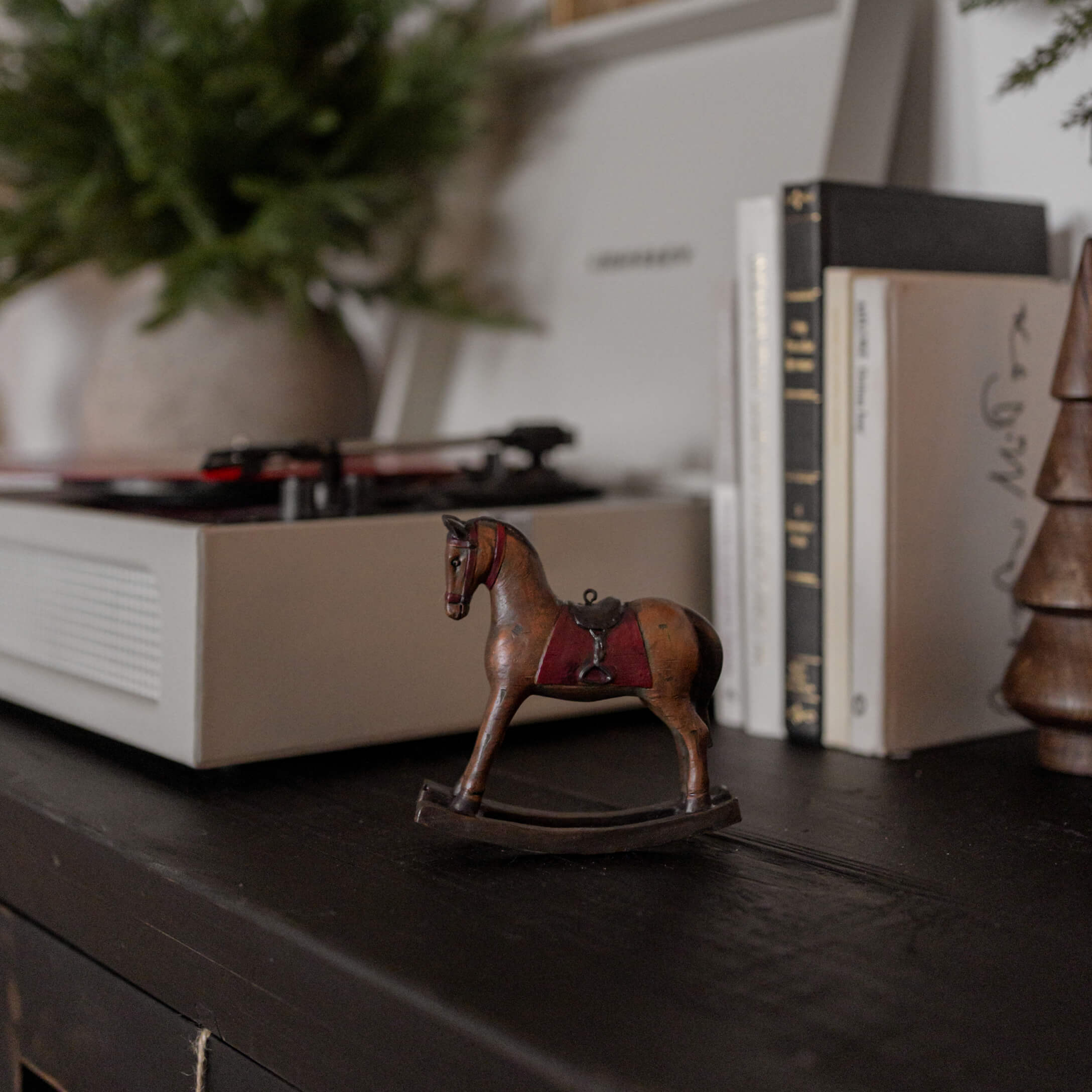 Caballo balancín de madera marrón con silla roja sobre superficie negra junto a libros y tocadiscos