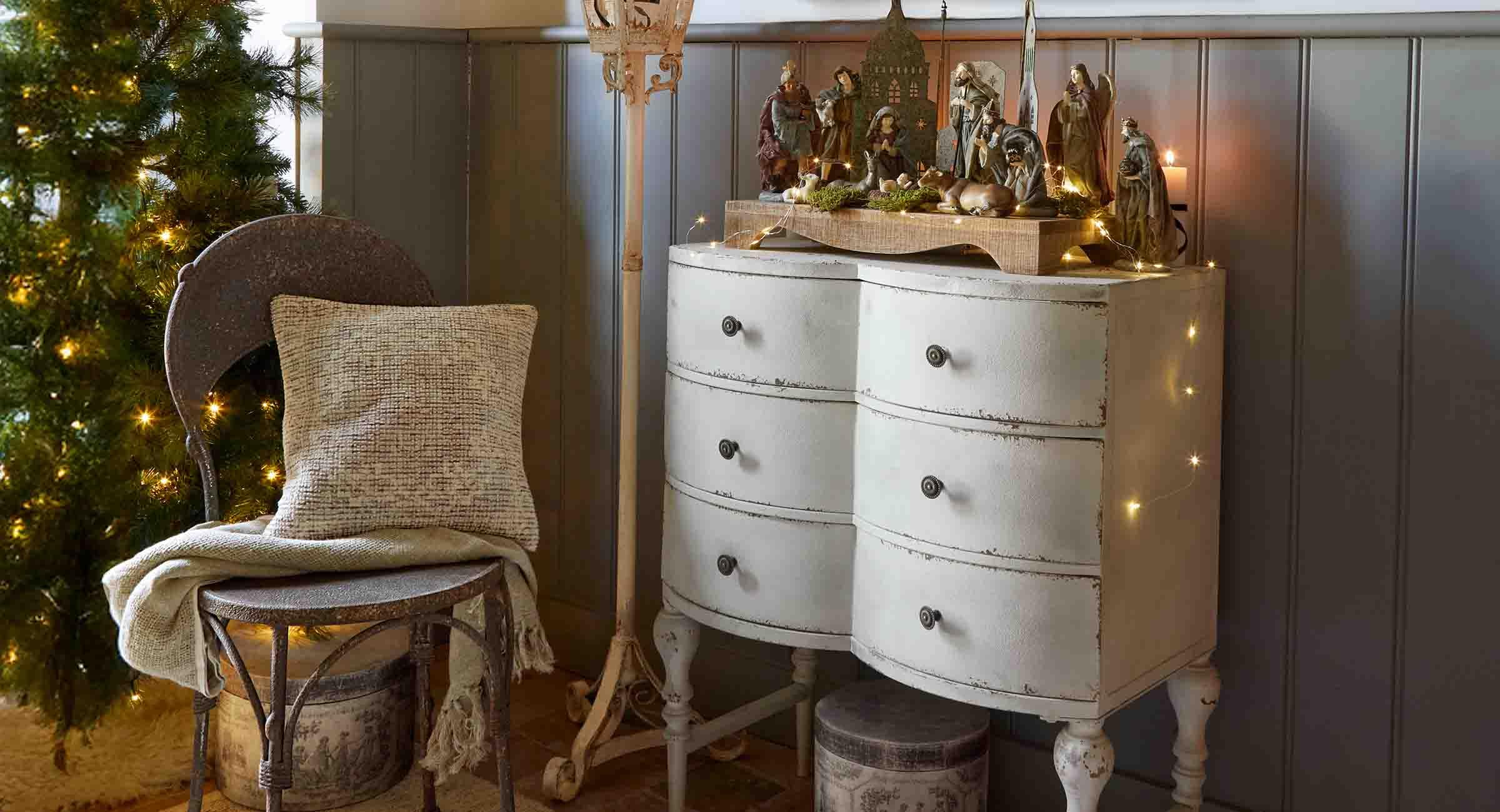 Cómoda blanca envejecida con belén de madera y decoración navideña en un ambiente acogedor