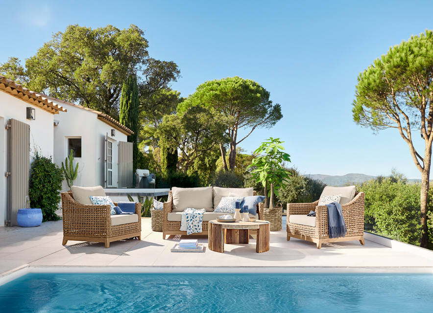 Conjunto de muebles de ratán beige junto a la piscina en terraza con vistas a árboles y cielo azul