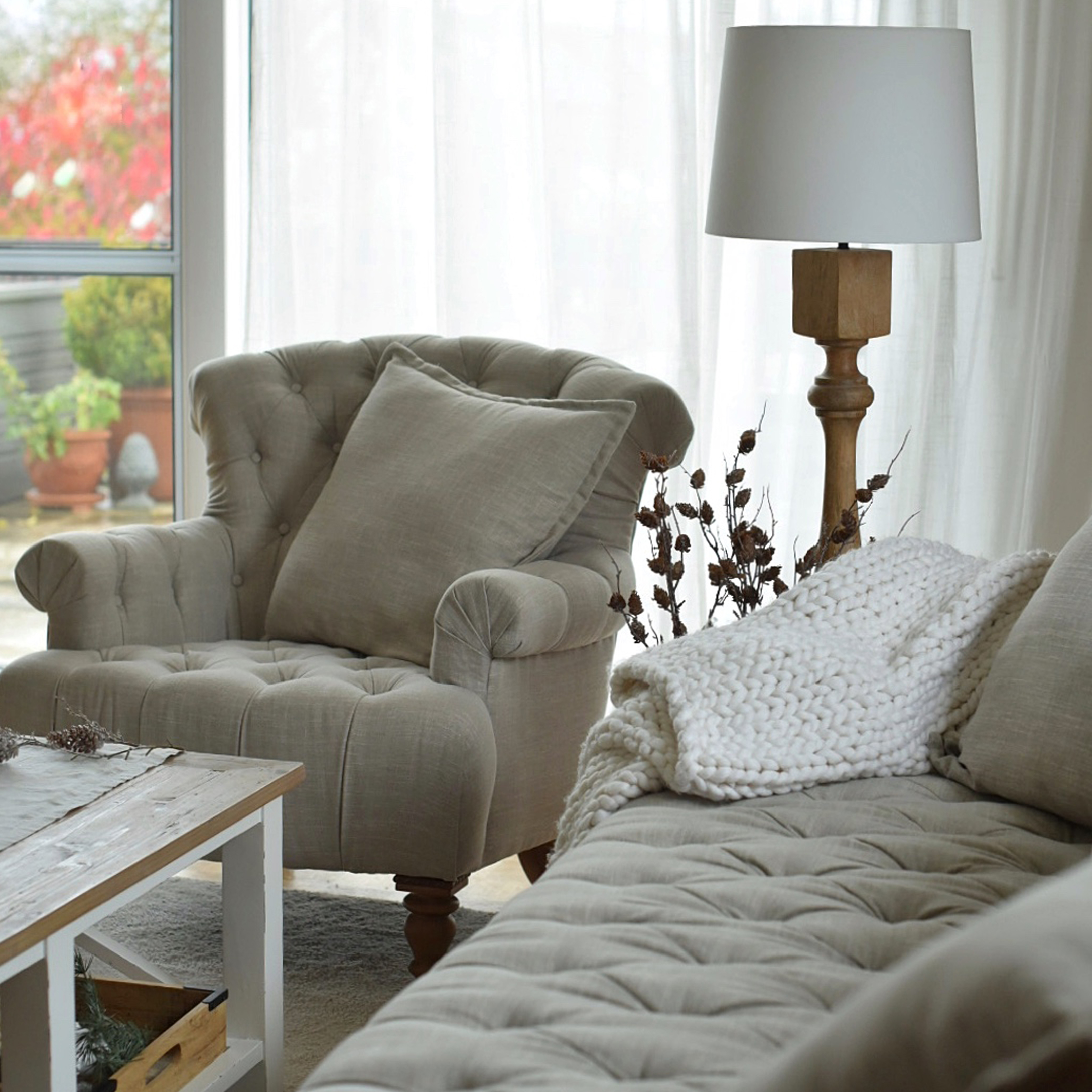 Sillón y sofá tapizados beige con cojines y manta blanca de punto en salón acogedor