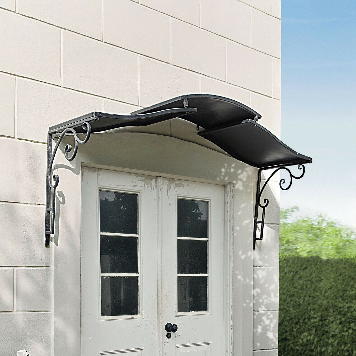 Tejadillo Trelonne Toldo metálico negro con soportes decorativos sobre puerta blanca de doble hoja con ventanas