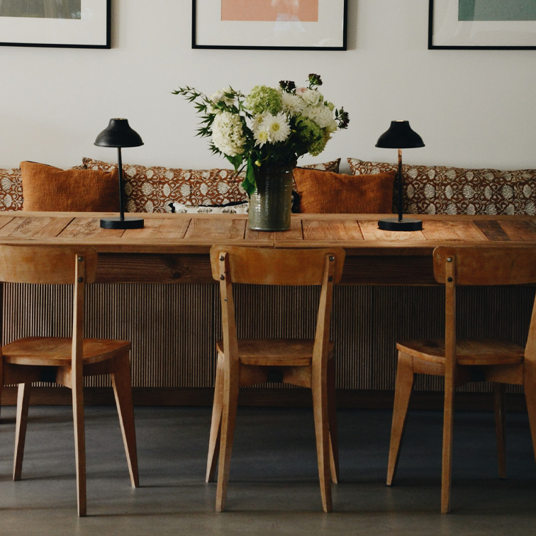 Mesa de madera con tres sillas, lámparas negras y jarrón con flores blancas en sala acogedora