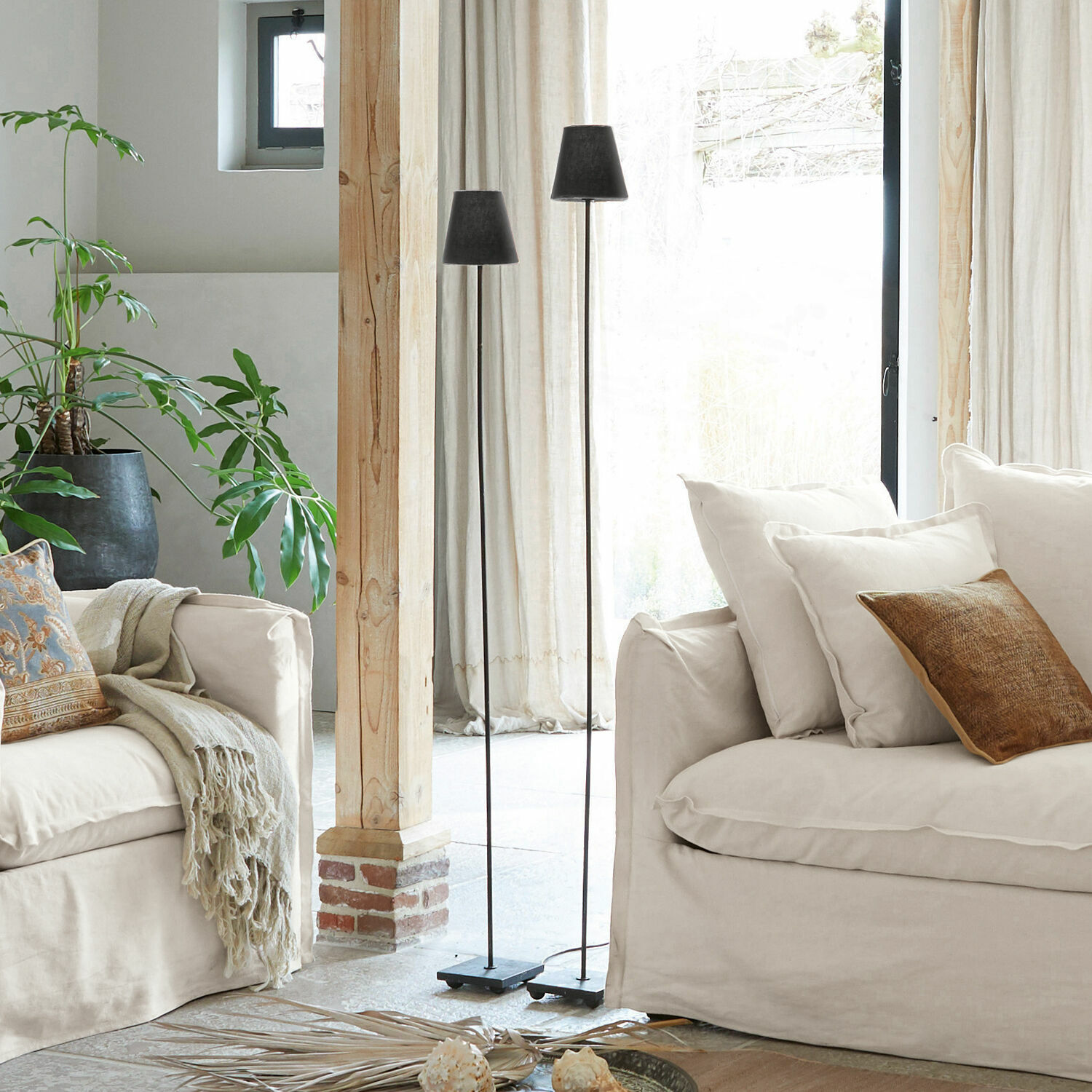 Dos lámparas de pie negras de metal en sala luminosa con sofá beige y planta verde