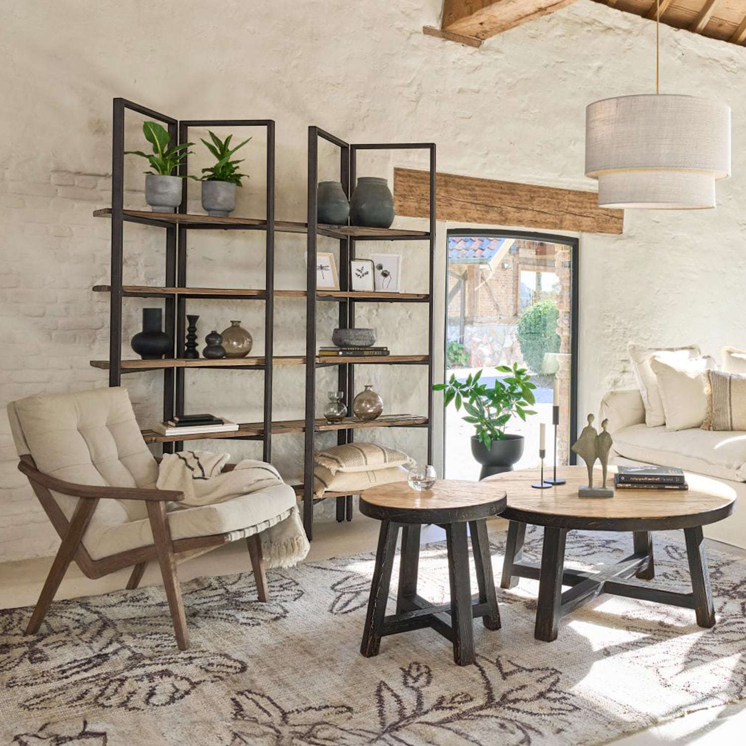 Salón acogedor con sillón de madera, estantería de metal y madera, mesas de centro redondas sobre alfombra decorativa