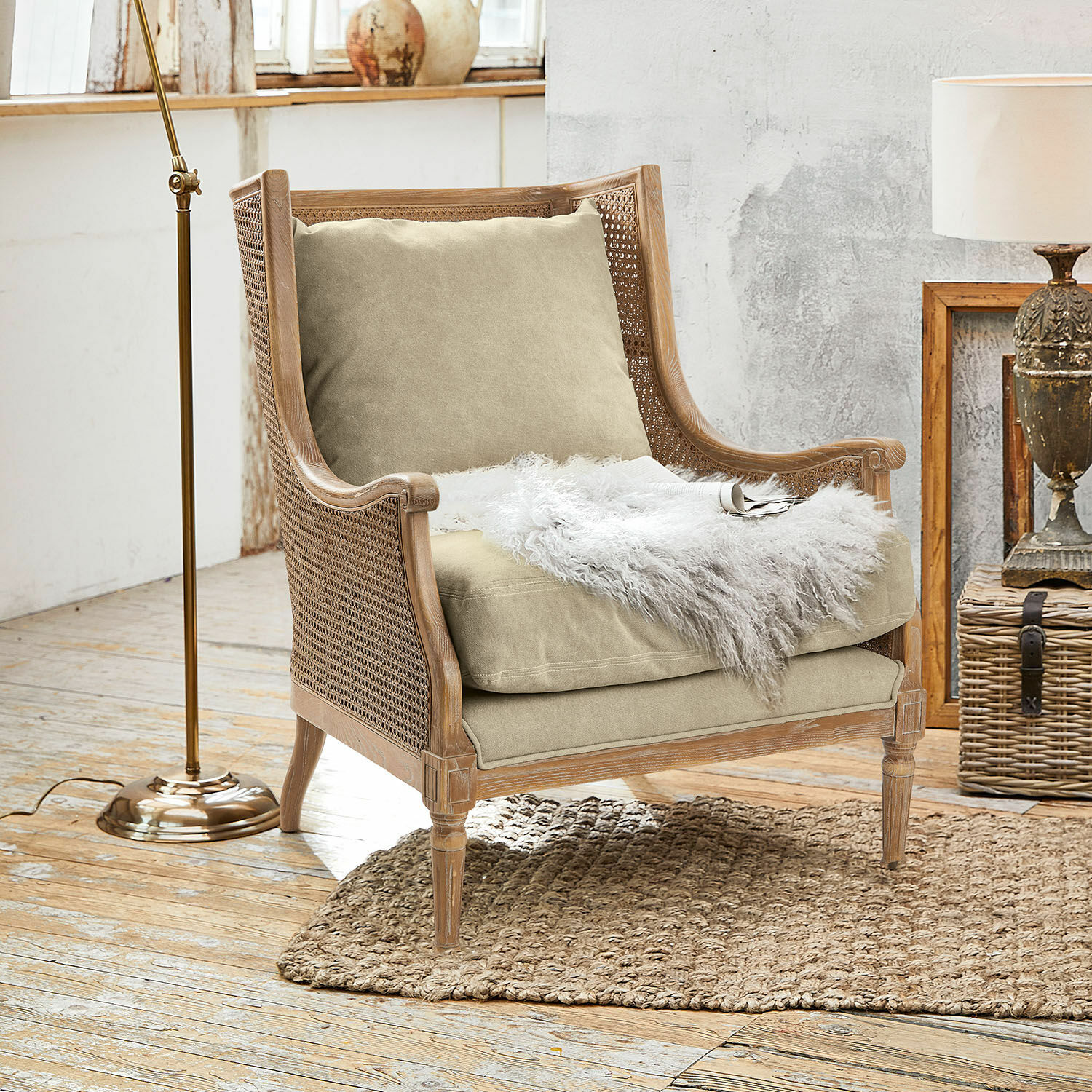 Sillón Greenbrier Sillón de madera y ratán con cojín beige y manta blanca de piel sobre alfombra natural