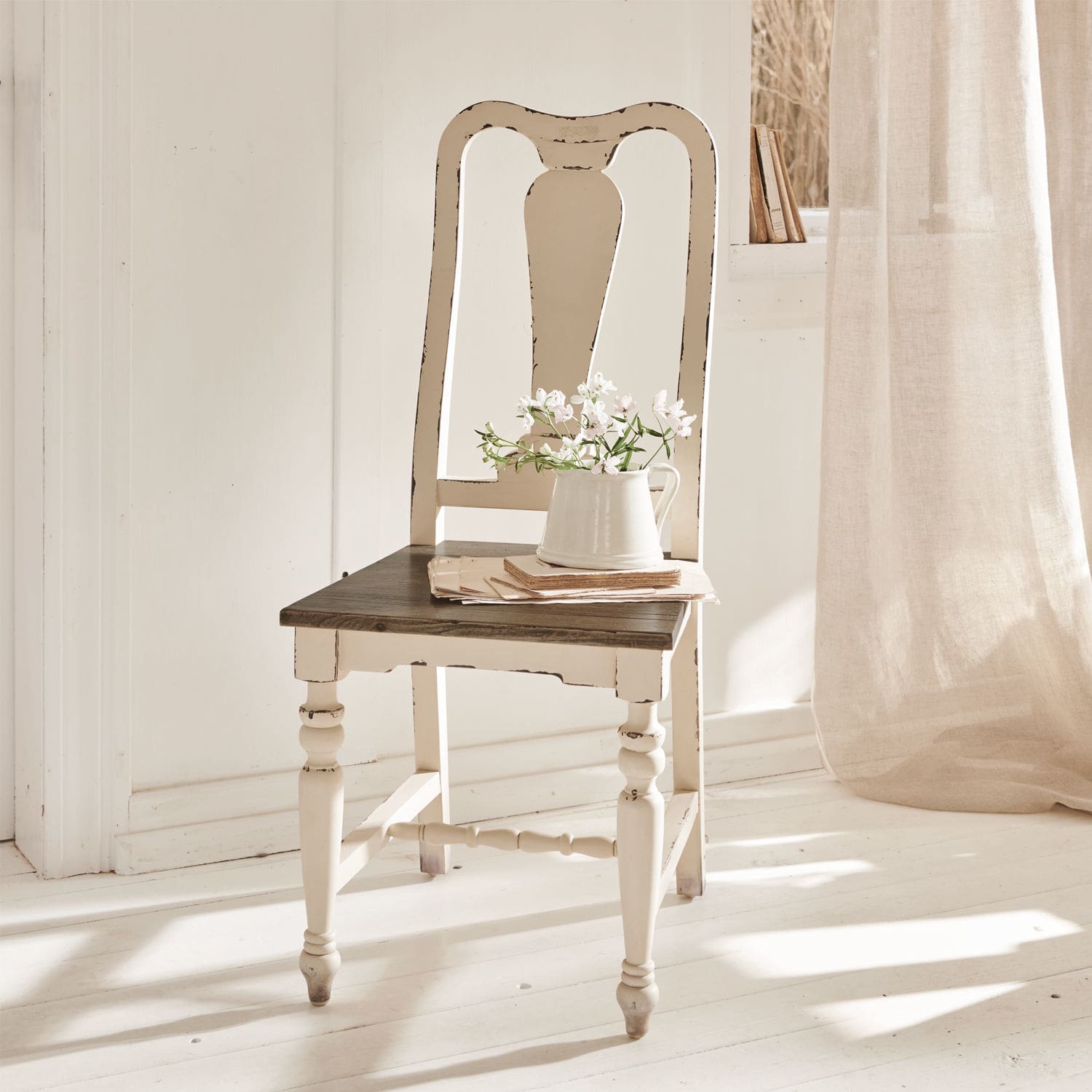 Silla Harry Silla vintage de madera blanca con asiento oscuro y jarra con flores en habitación luminosa