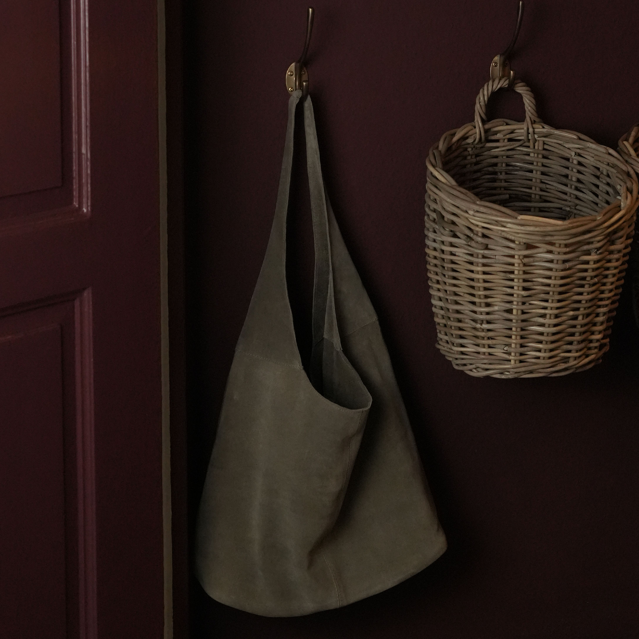 Delantal gris de ante colgado en gancho de cobre junto a cesta de mimbre en pared oscura
