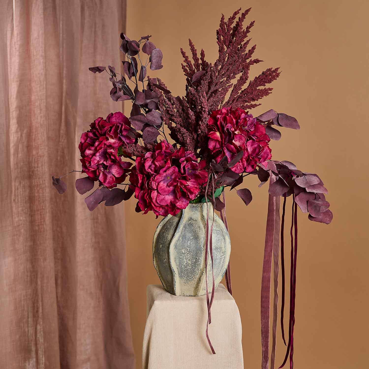 Ramo de flores artificiales burdeos en jarrón de cerámica sobre fondo beige, decoración de interiores