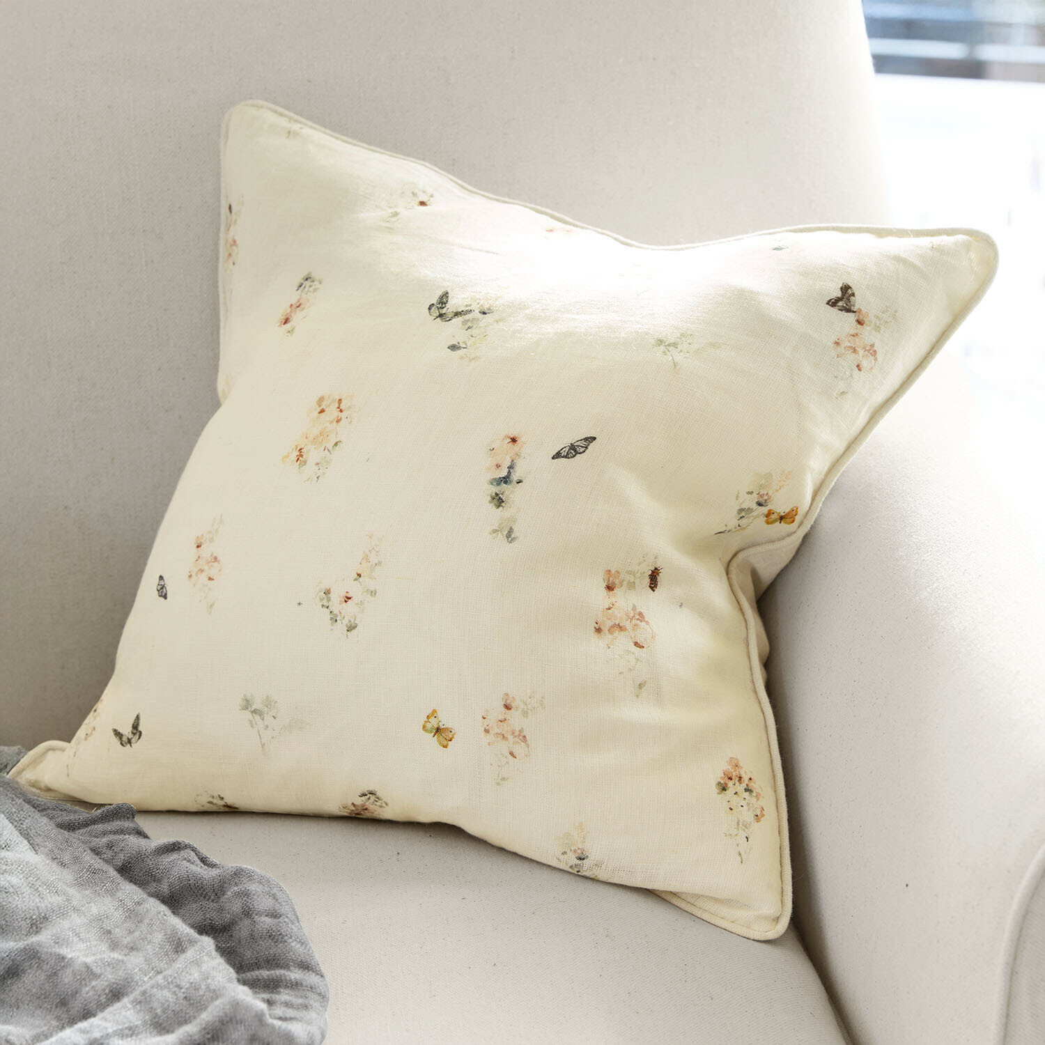 Funda de cojín Salénaïs Cojín color crema claro con delicado estampado de flores y mariposas sobre sofá, decoración de interiores