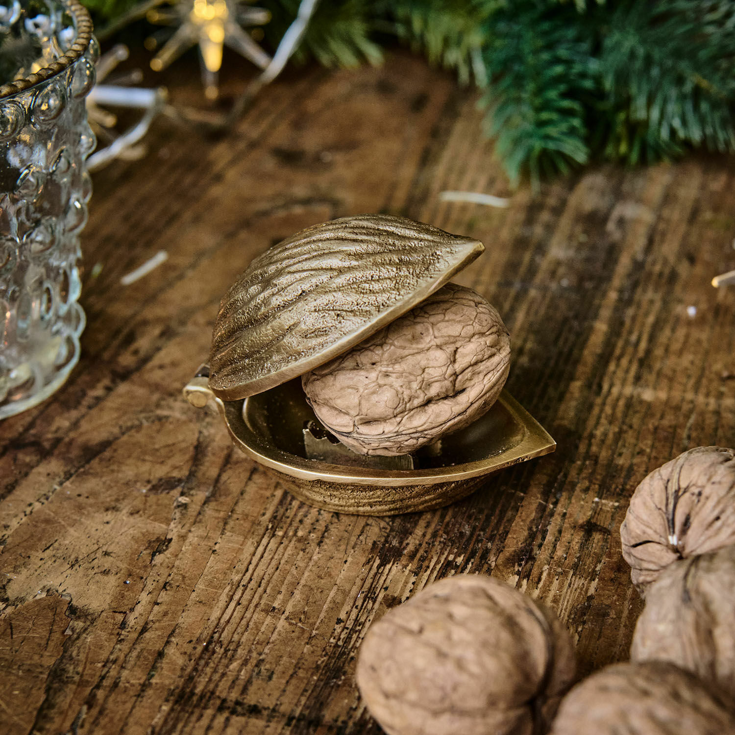 Cascanueces Swansea Cascanueces metálico dorado con forma de nuez sobre mesa de madera con nueces naturales