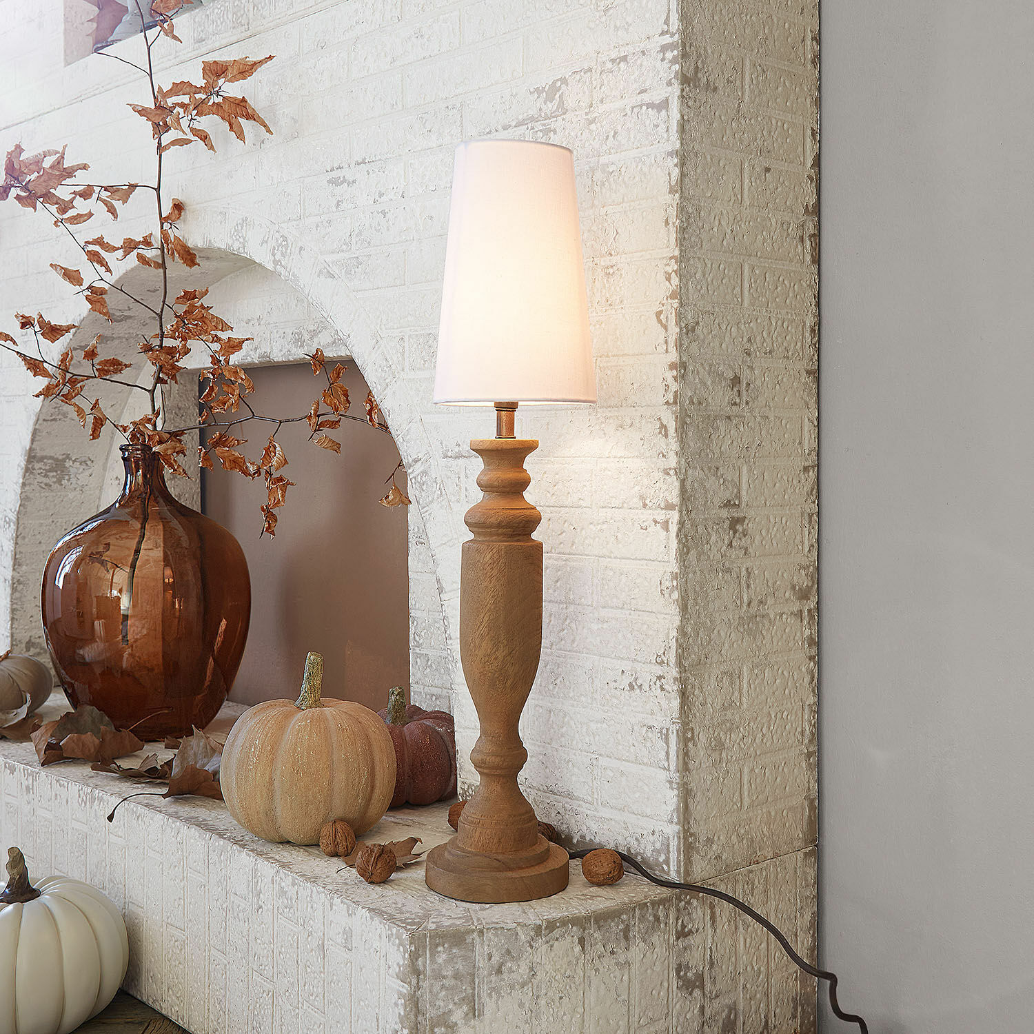 Lámpara de mesa Ambrevaux Lámpara de mesa de madera con pantalla blanca frente a pared de ladrillo blanco y decoración otoñal