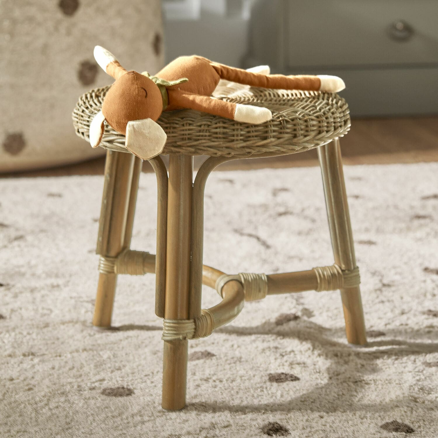 Taburete Dunley Taburete de ratán color natural con peluche sobre alfombra suave en habitación infantil
