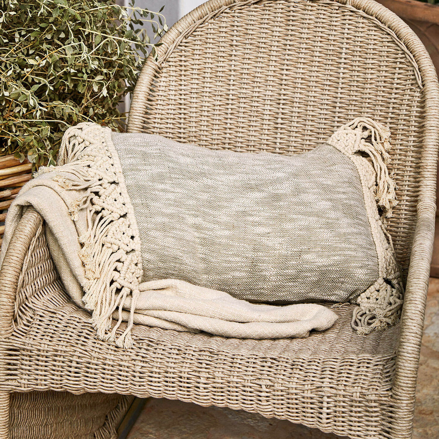 Funda de cojín Dunlora Manta beige con flecos sobre silla de mimbre, decoración acogedora para el hogar