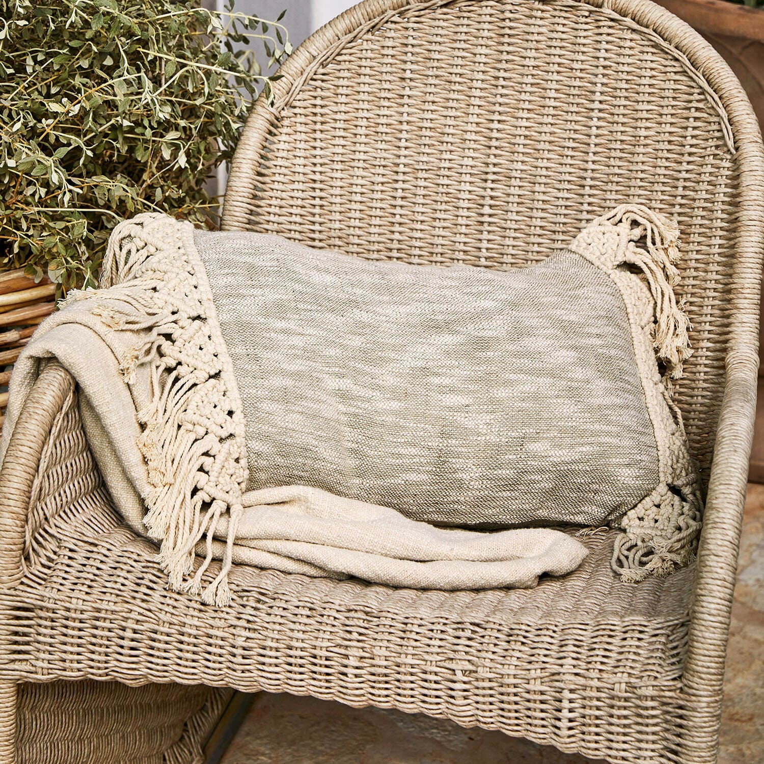 Funda de cojín Dunlora Manta beige con flecos sobre silla de mimbre, decoración acogedora para el hogar