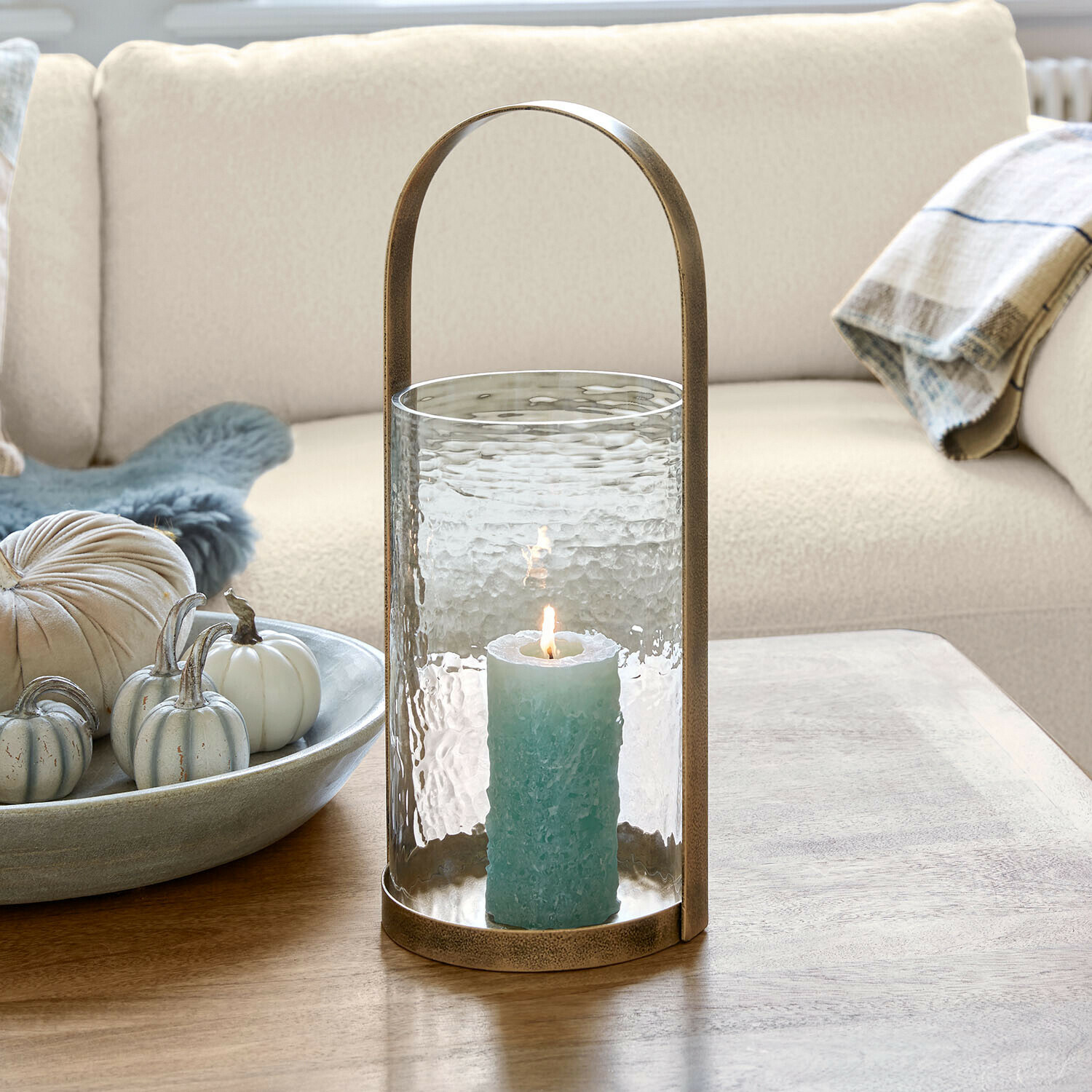 Portavelas Omirah Linterna de cristal con asa de latón y vela azul sobre mesa de madera en salón